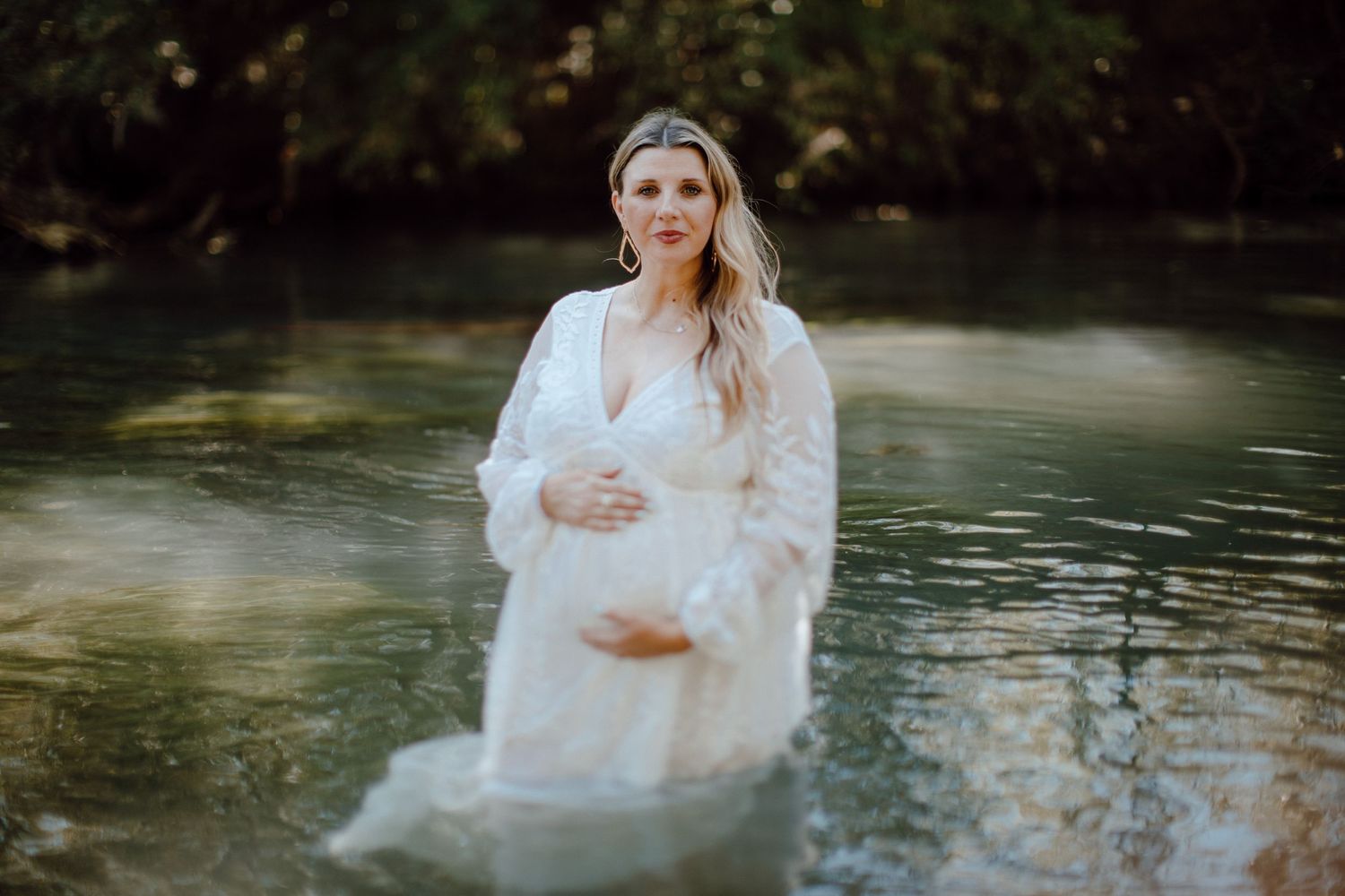 A woman in white dress standing in ethereal water for maternity photo.