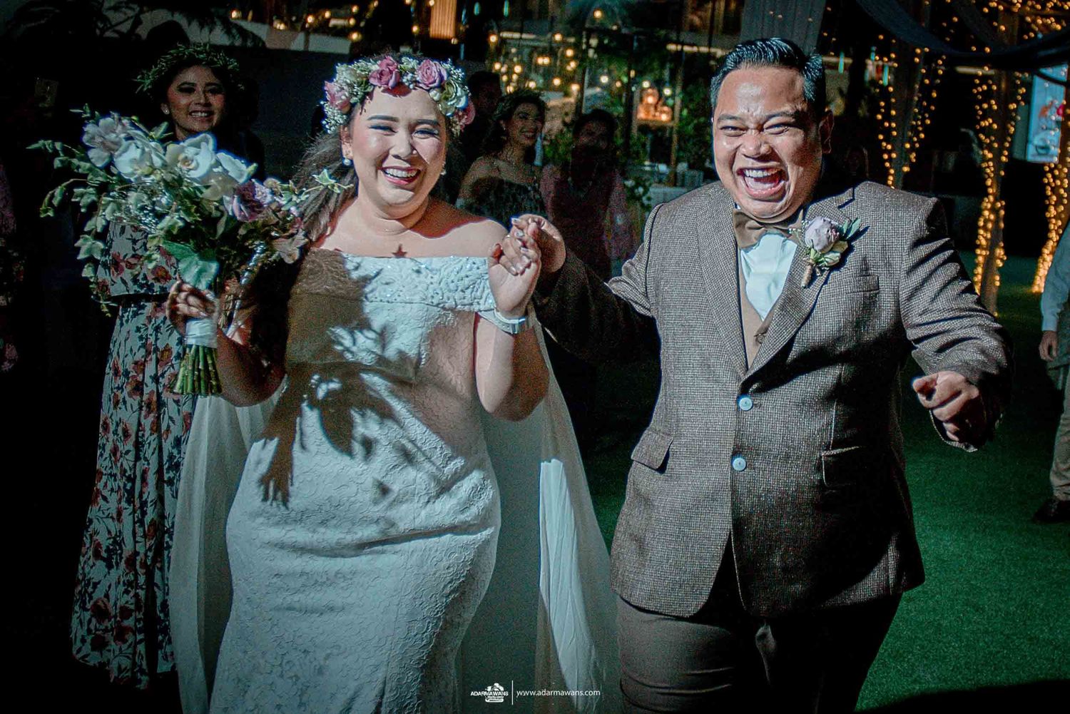 Couple dancing together at evening wedding reception with festive lights in background.