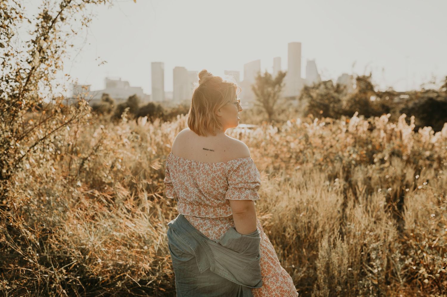 Person in vintage dress looking towards city skyline through golden autumn field.