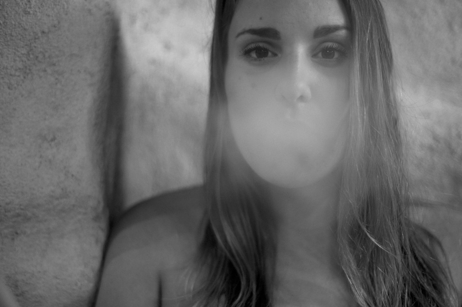 Artistic black and white portrait of someone blowing a cloud of smoke against a wall.