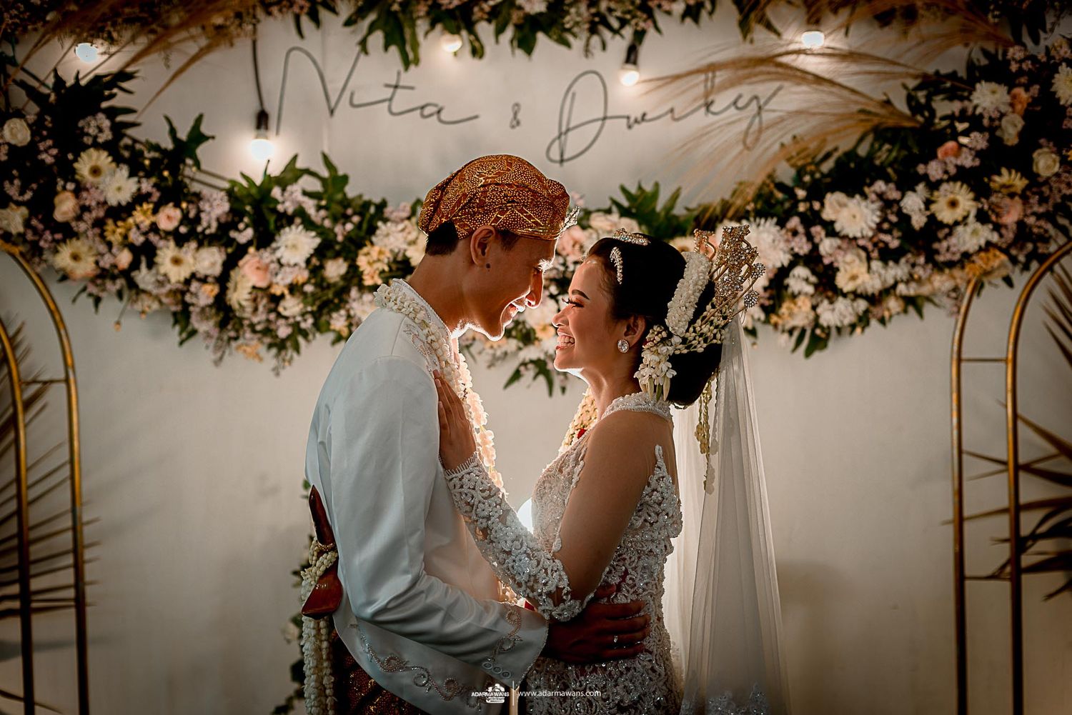 Newlyweds sharing intimate moment under floral arch with romantic lighting.