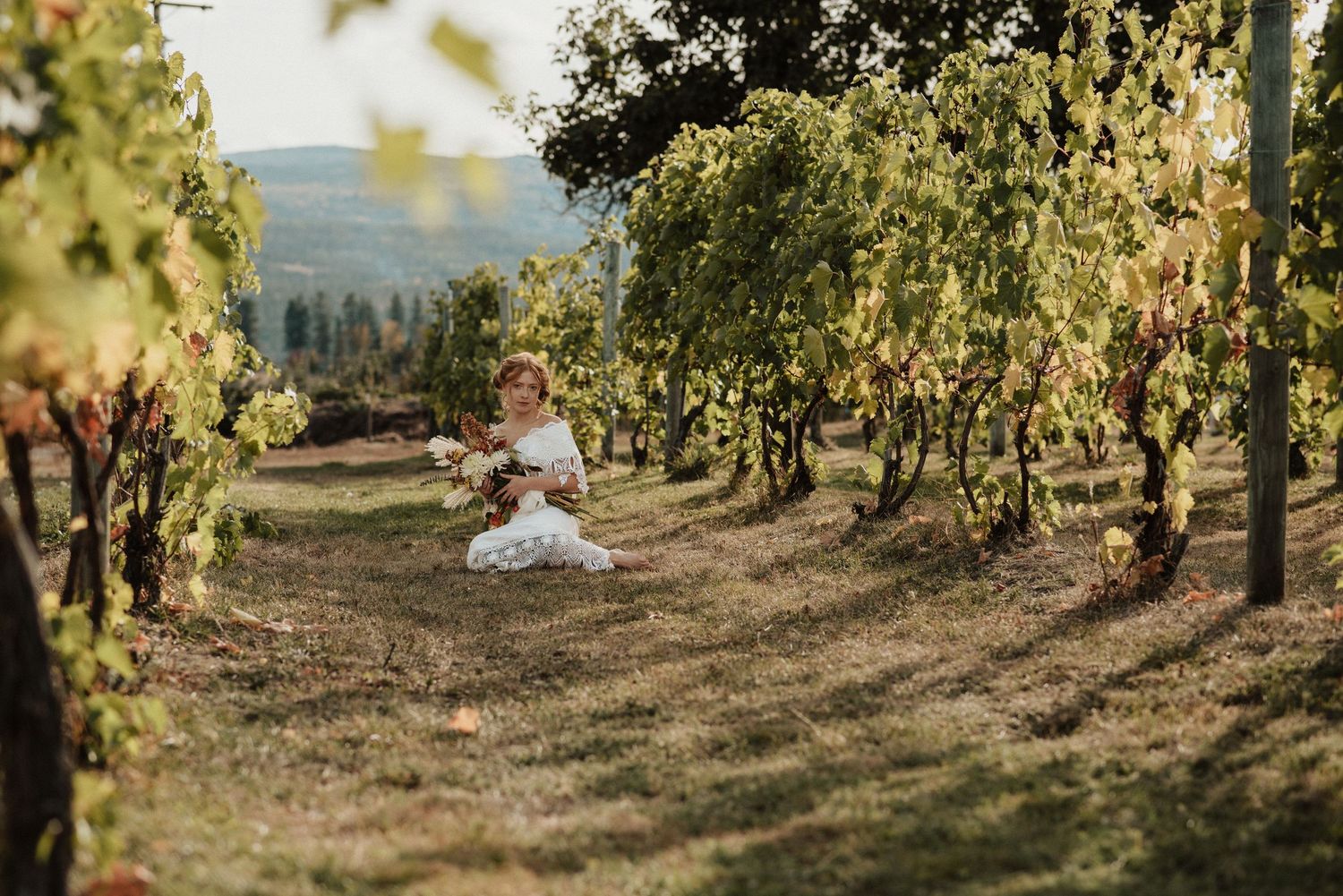 Kelowna Bridal portraits. Bride sits in the grass in a vineyard