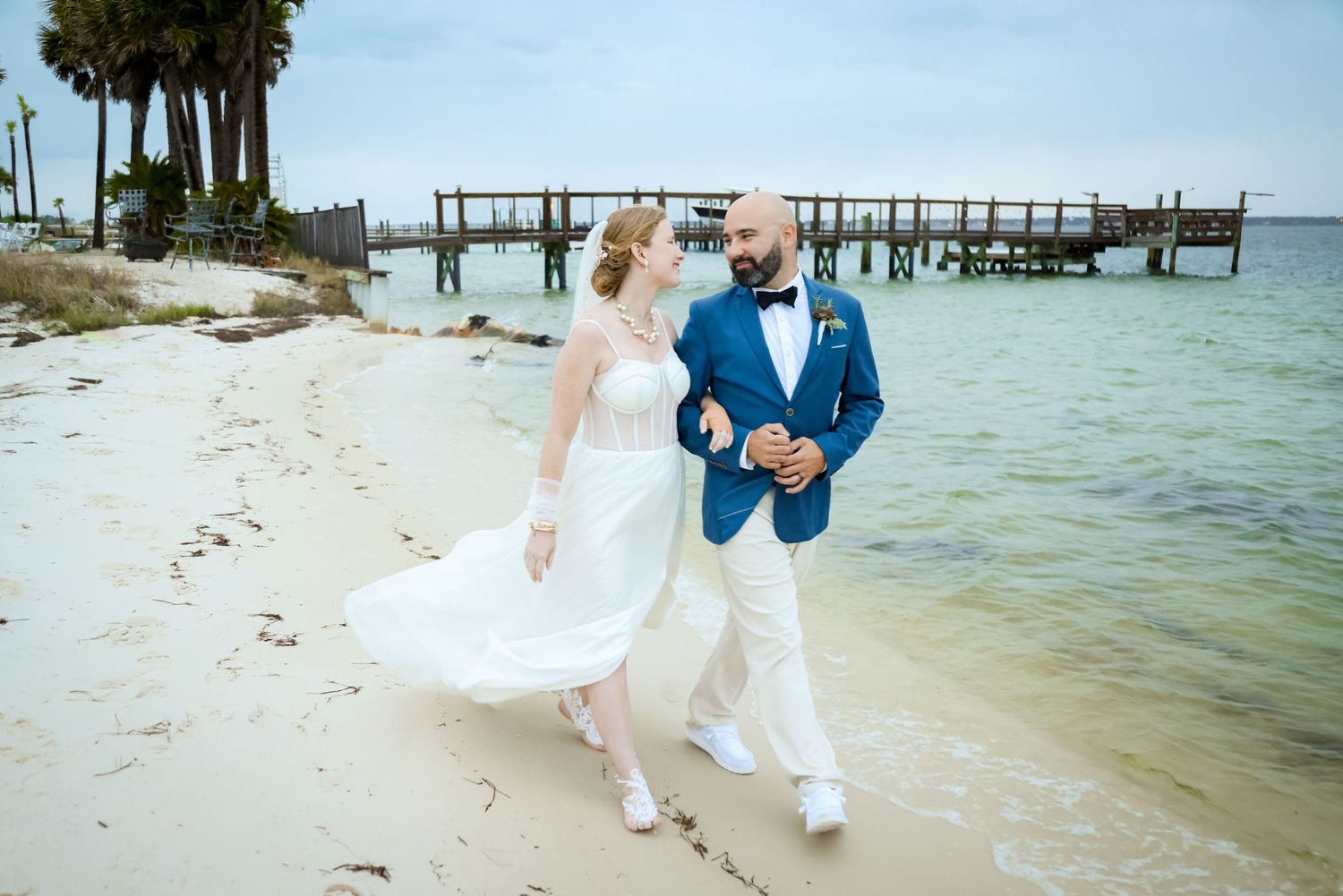 A joyful beach wedding photo with a wooden pier in the background.