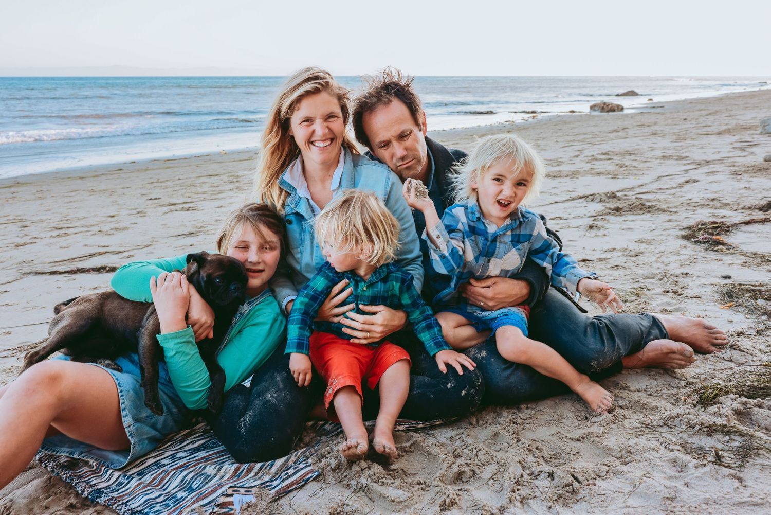 Family enjoying a playful moment together while sitting on a blanket at the beach.