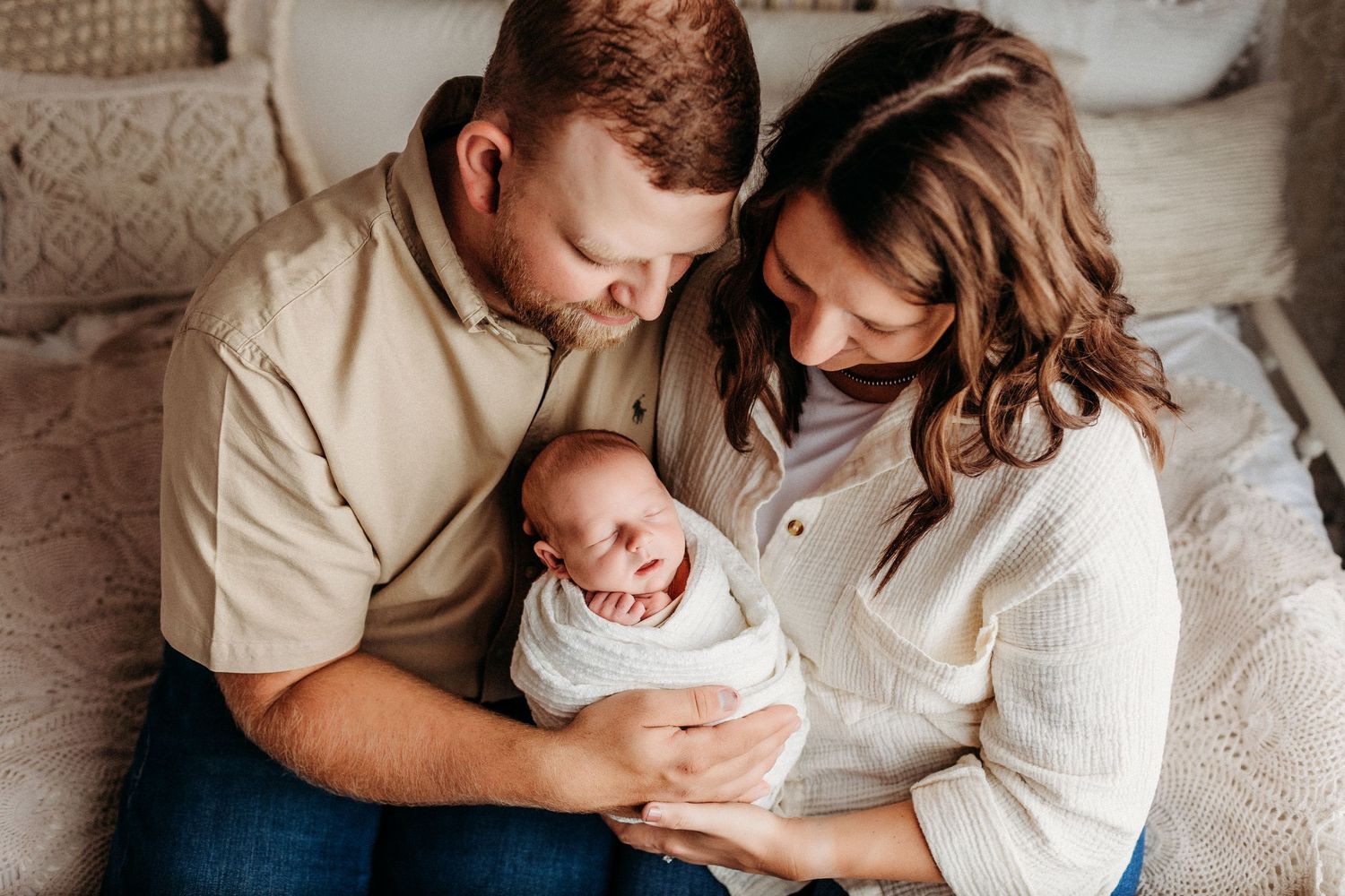 Intimate family moment with parents holding newborn baby on couch.