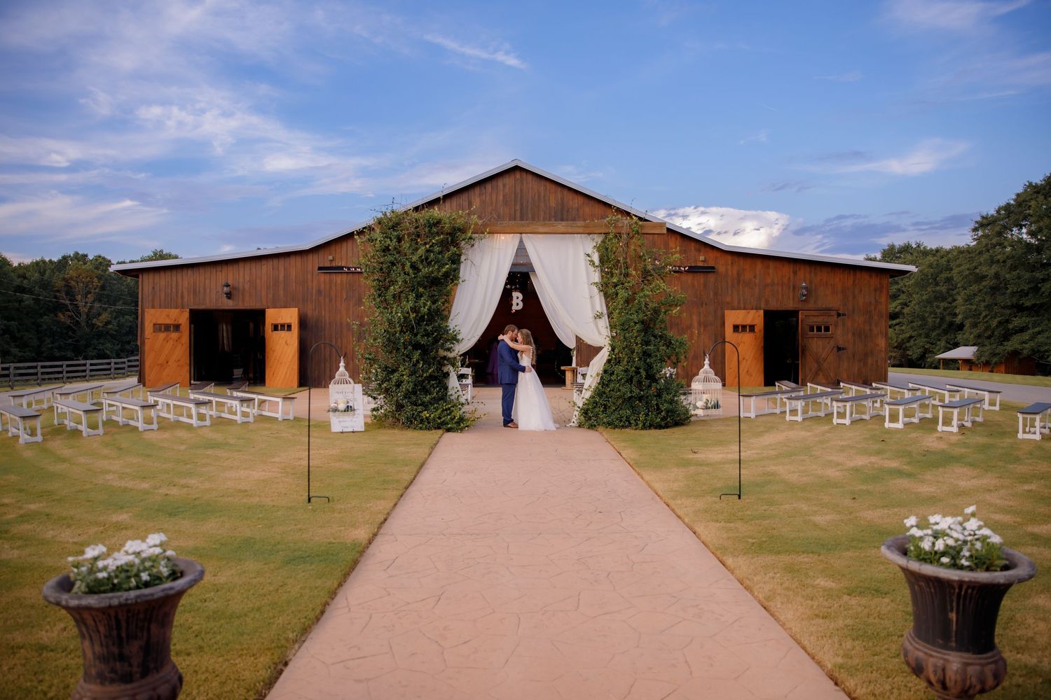 Rustic barn wedding venue with white draping and rows of ceremony chairs on a manicured lawn.