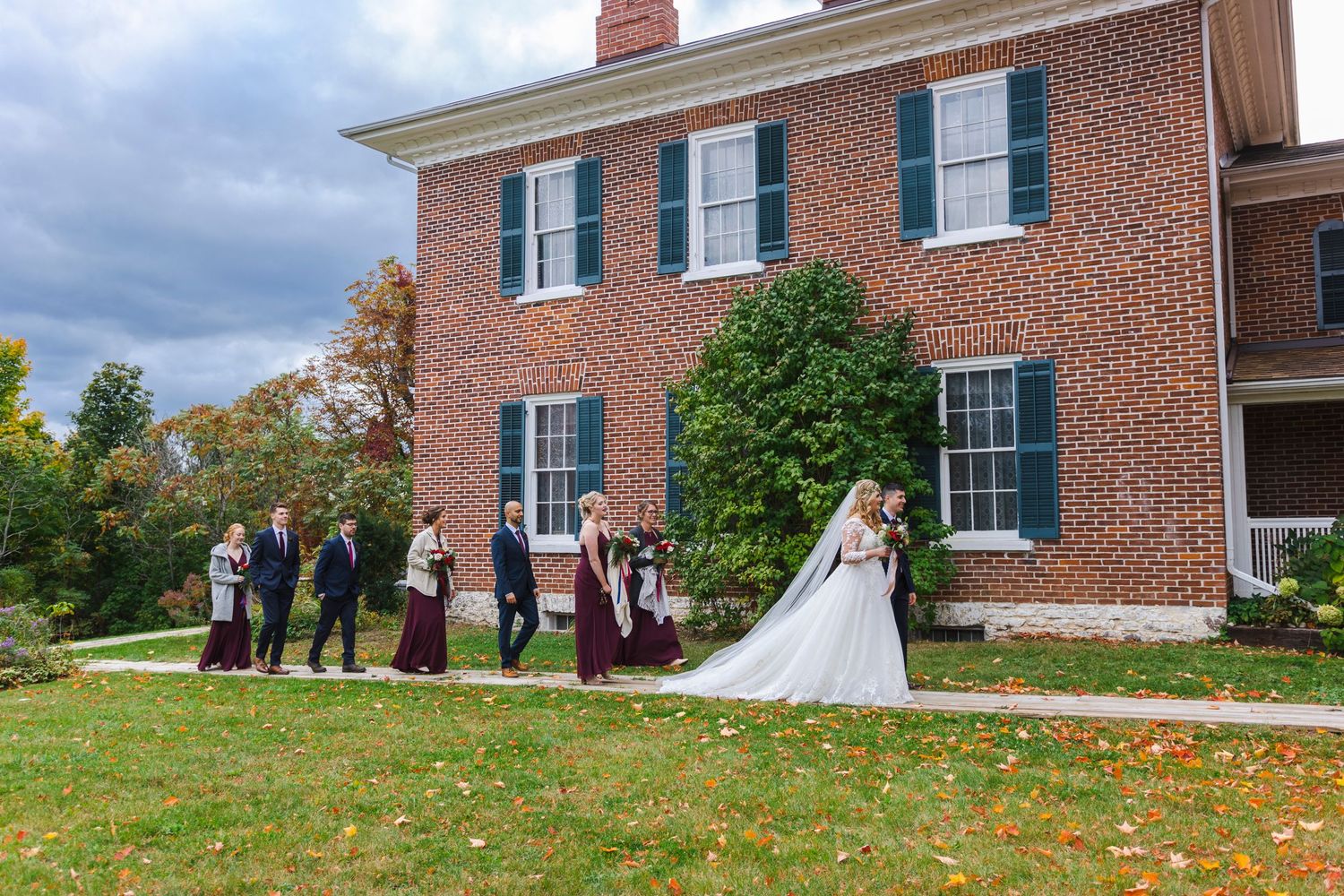 Wedding party gathered outside historic brick mansion with white columns.