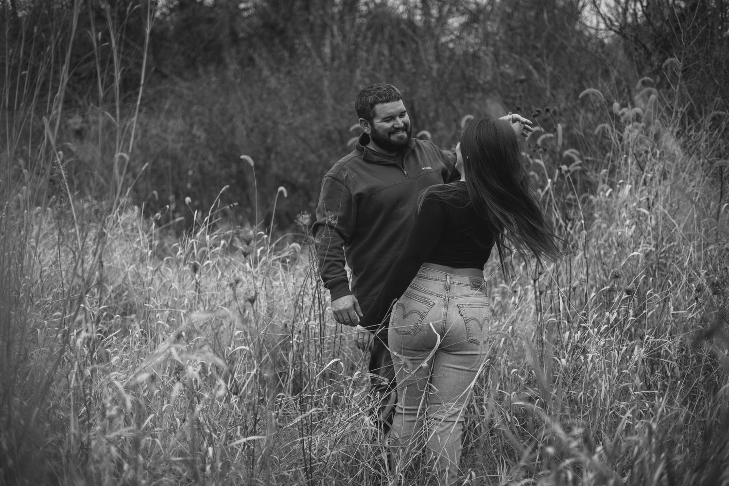 Black and white portrait of couple embracing in a field of tall grass and wildflowers.