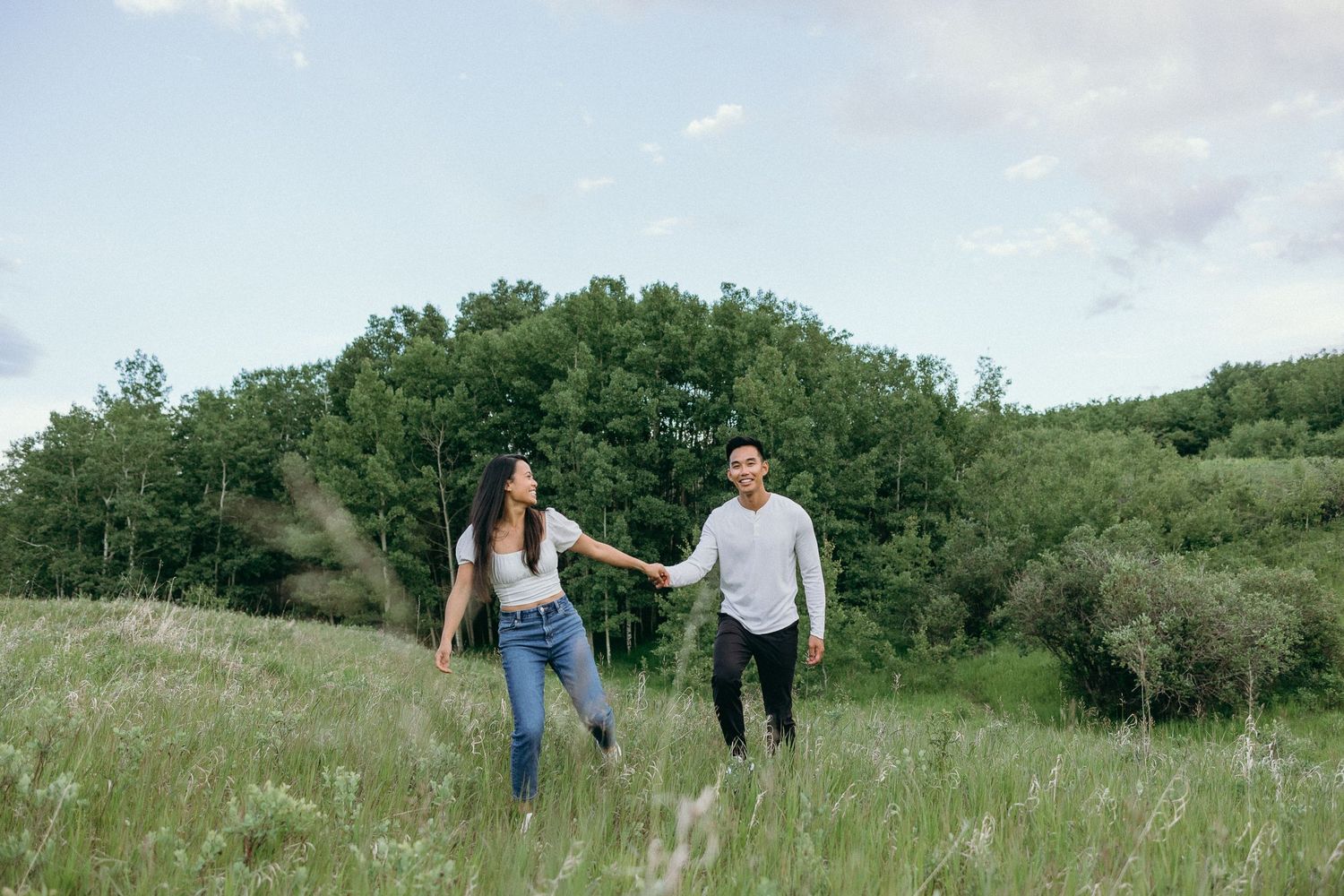 Couple walking through lush green prairie fields under bright summer sky.