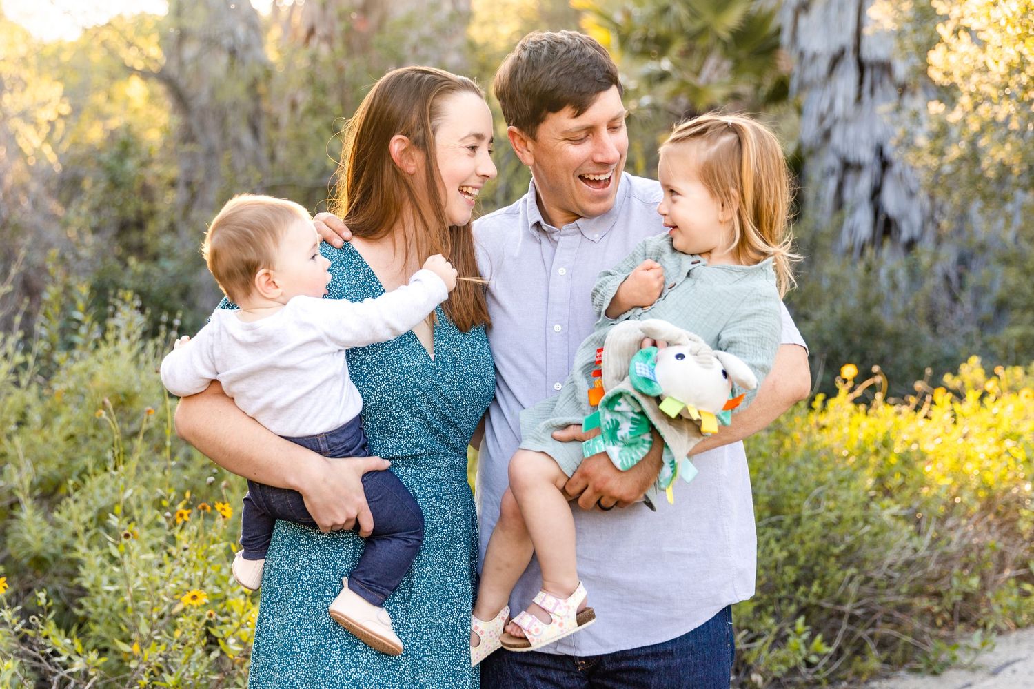 Happy family of four enjoying a sunny outdoor photo session in a natural setting with flowers.