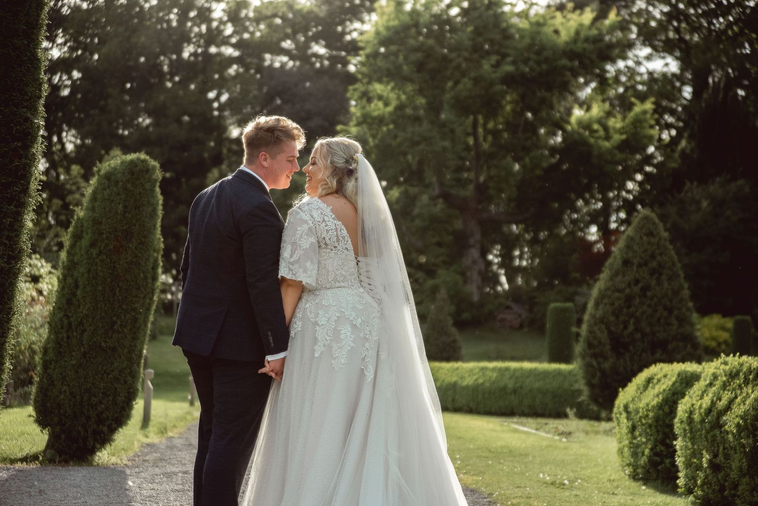 A couple shares an intimate moment in formal wedding attire amidst a lush garden setting.