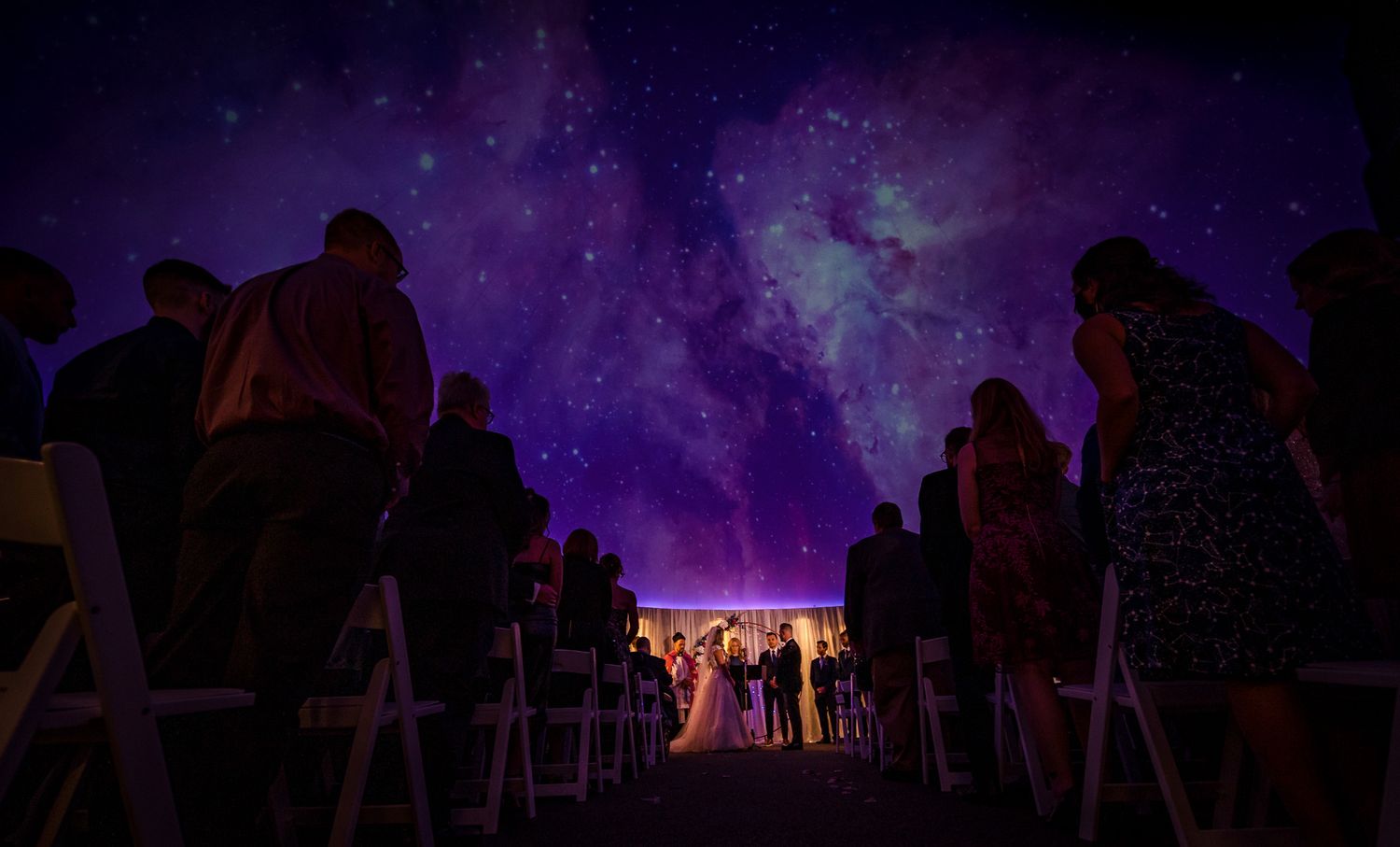 Silhouettes of wedding guests against a purple starlit sky at dusk.