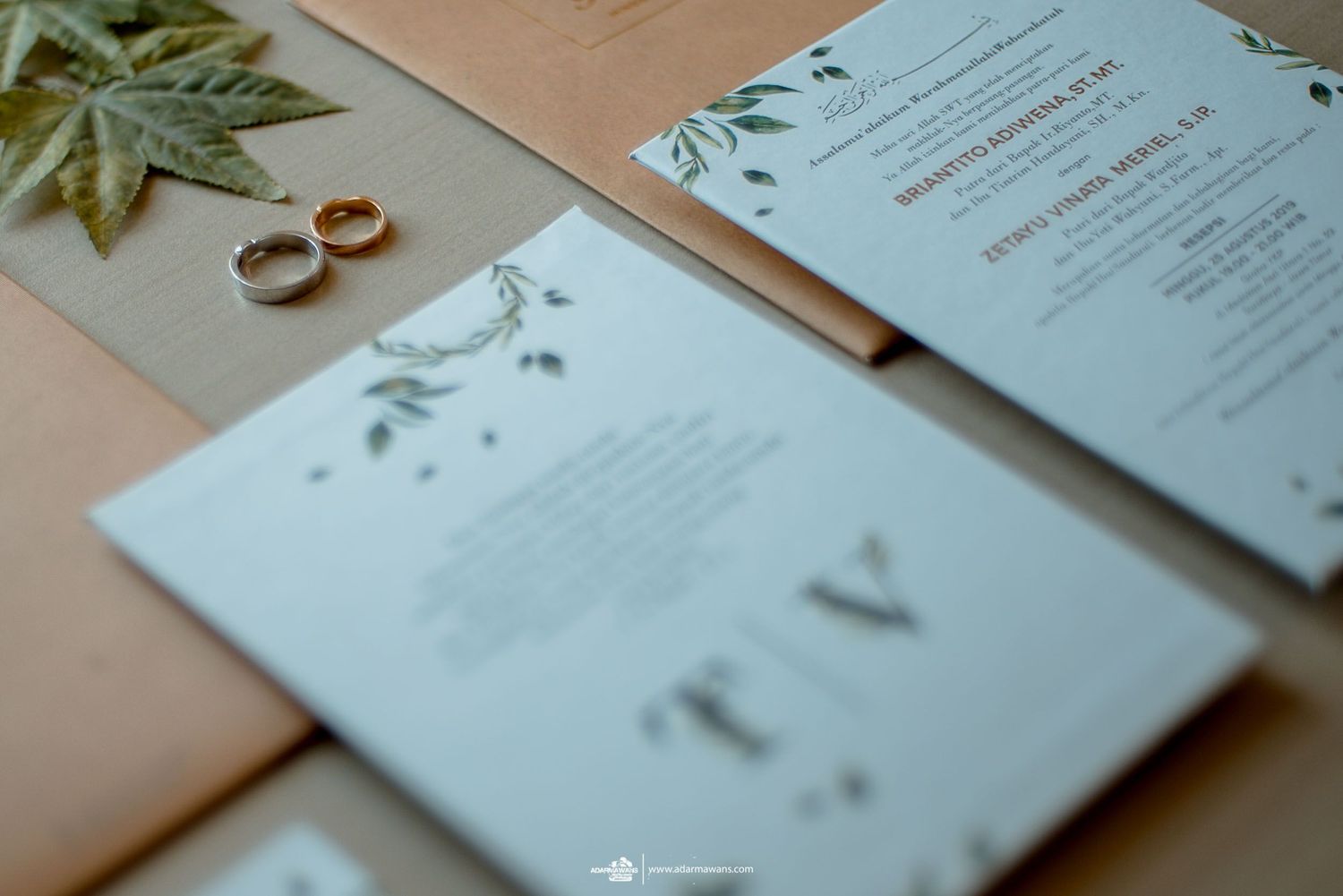 Elegant wedding invitations with floral designs and gold rings on peach-colored background.