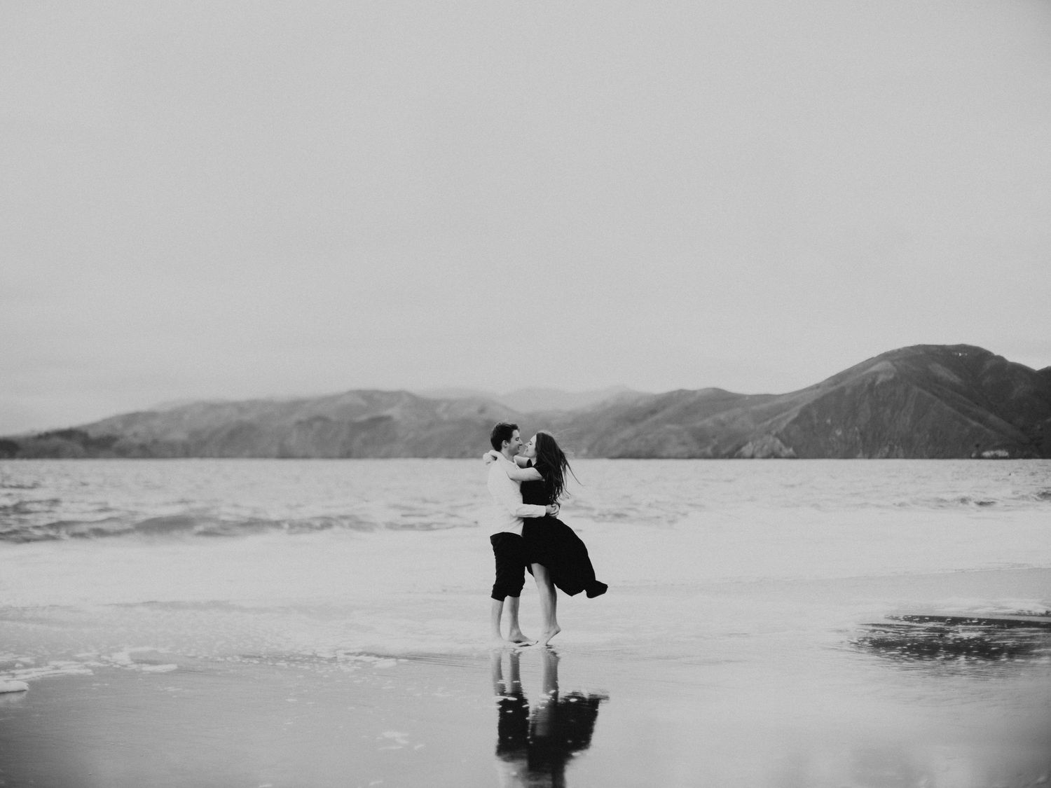 A couple embraces on a misty beach in black and white photography.