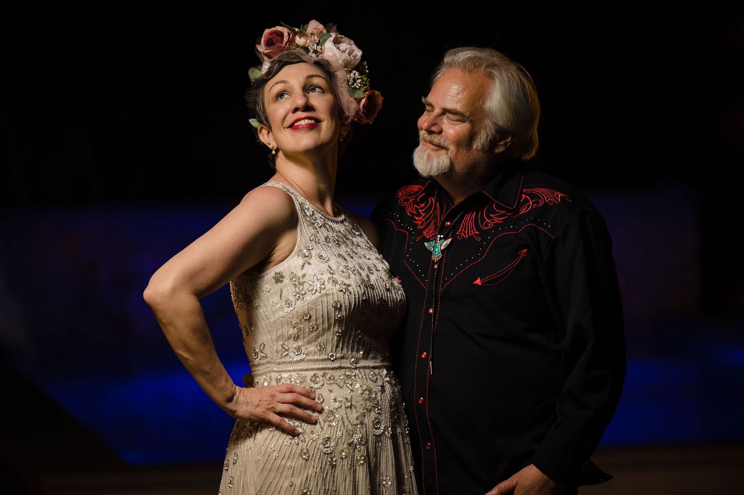 A theatrical scene showing performers in formal attire against a dark background.