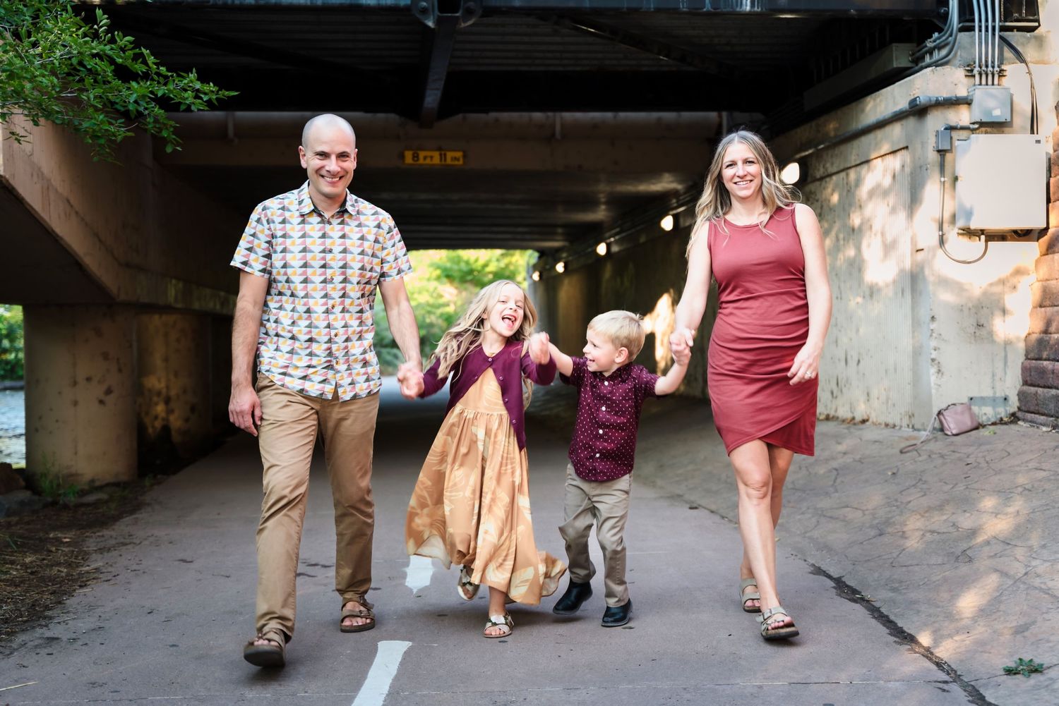 A family walks together holding hands under a bridge tunnel on a sunny day.