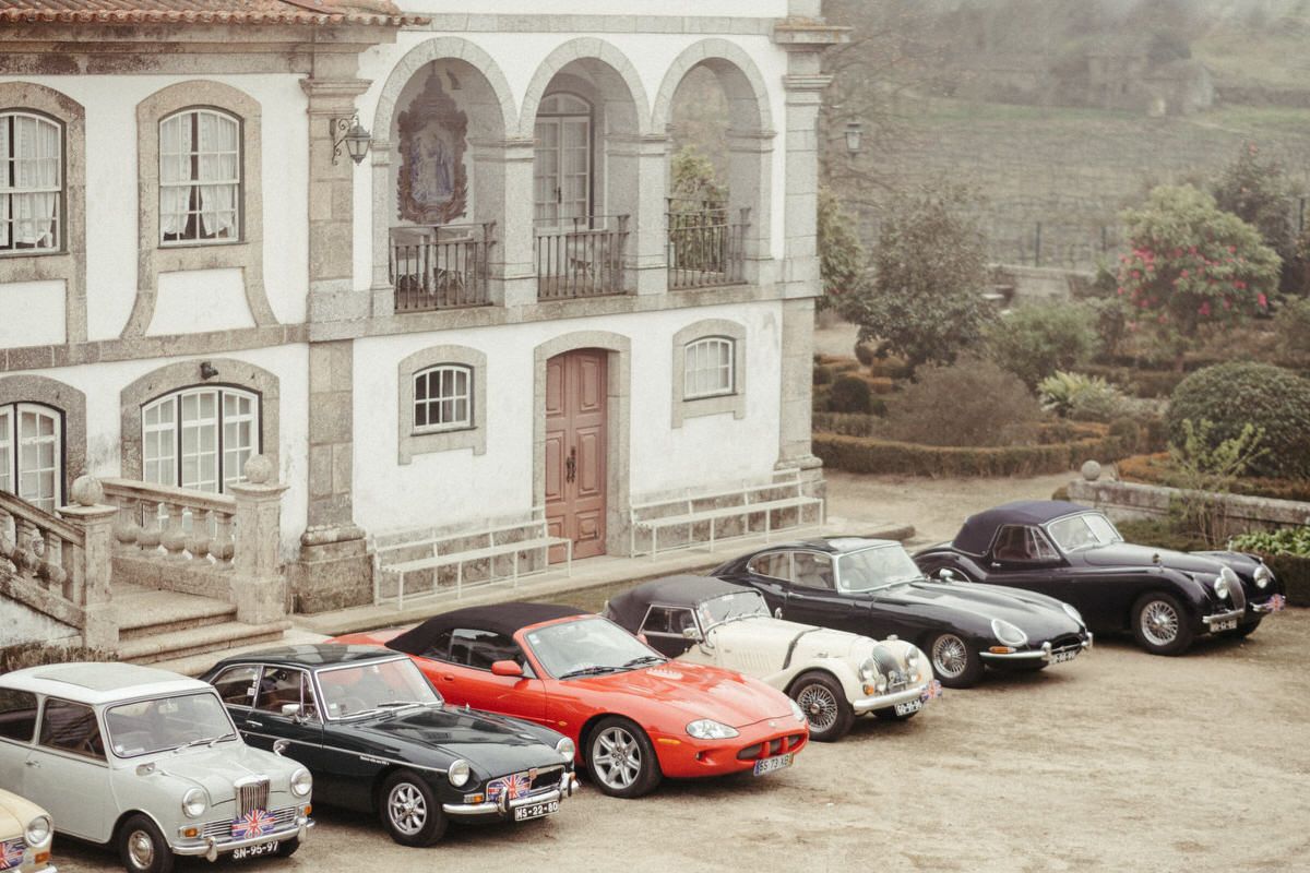 Vintage luxury cars parked in a row outside a classic stone building.