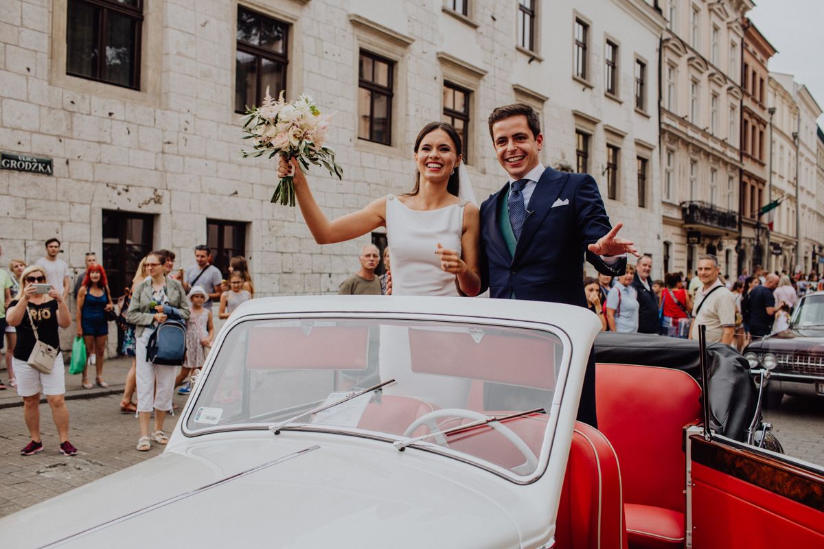 Happy newlyweds riding in a vintage red and white convertible car through the city.