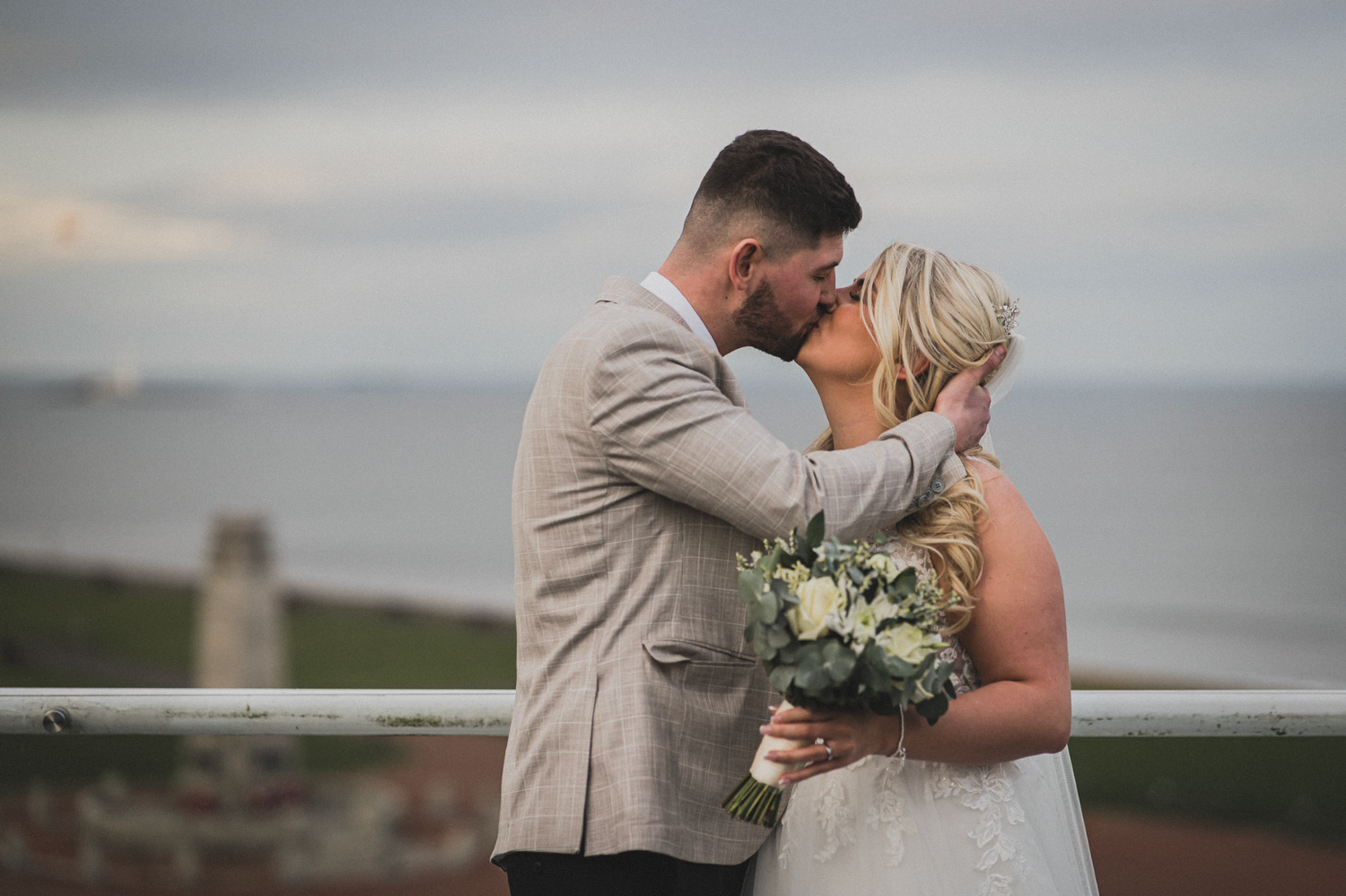 A romantic wedding moment with a bouquet of white flowers against a coastal backdrop.