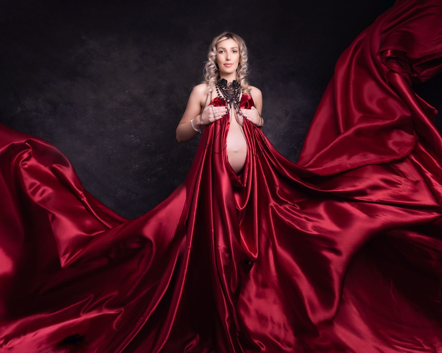 Dramatic fashion photo of flowing red silk dress against dark background.