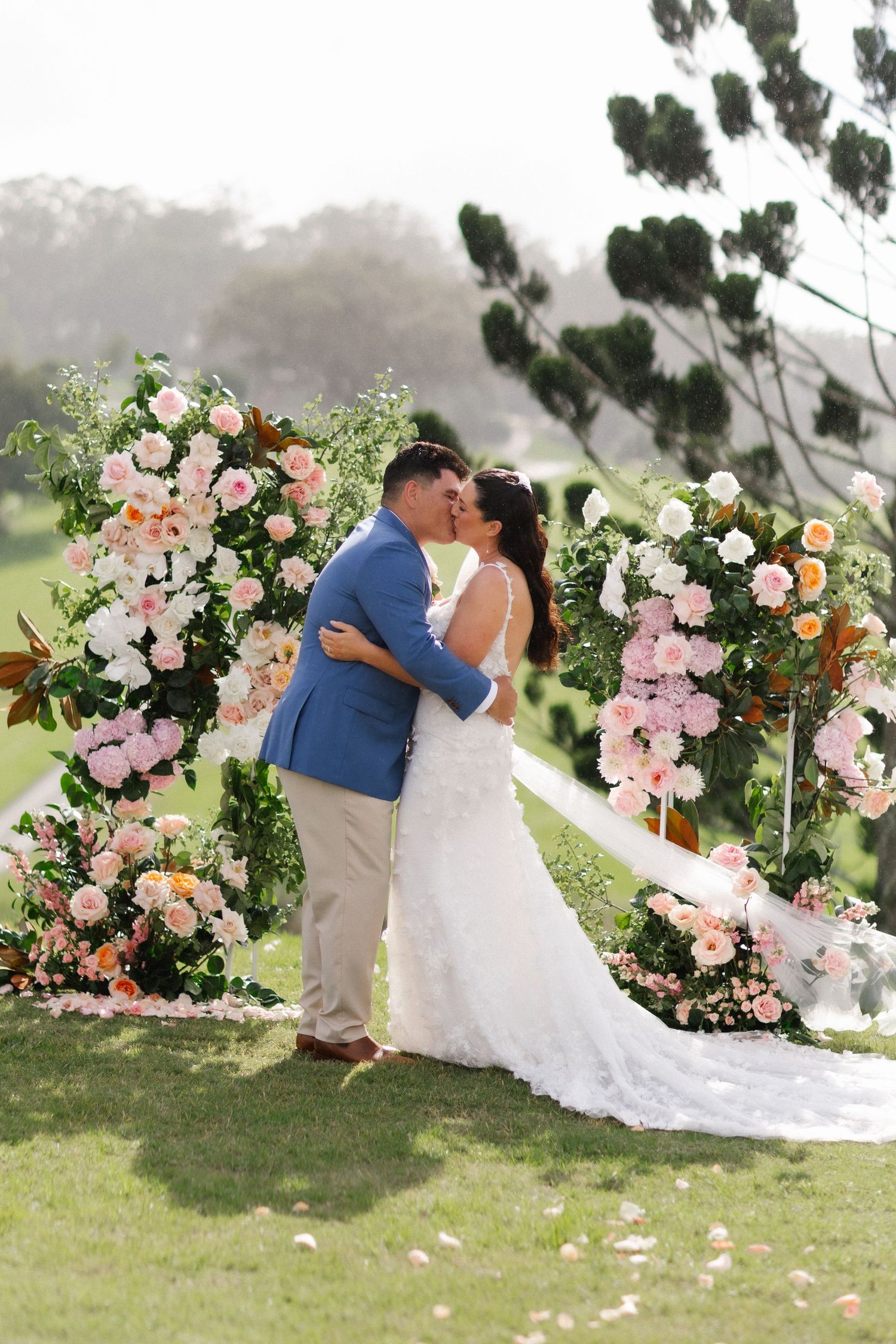 Couple exchanging vows outdoors at a floral arch wedding ceremony on a lush green golf course.
