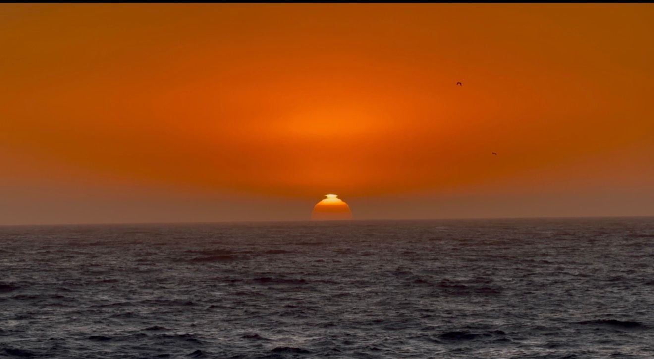 Stunning ocean sunset with vibrant orange sky as sun dips below the horizon over calm dark waters.