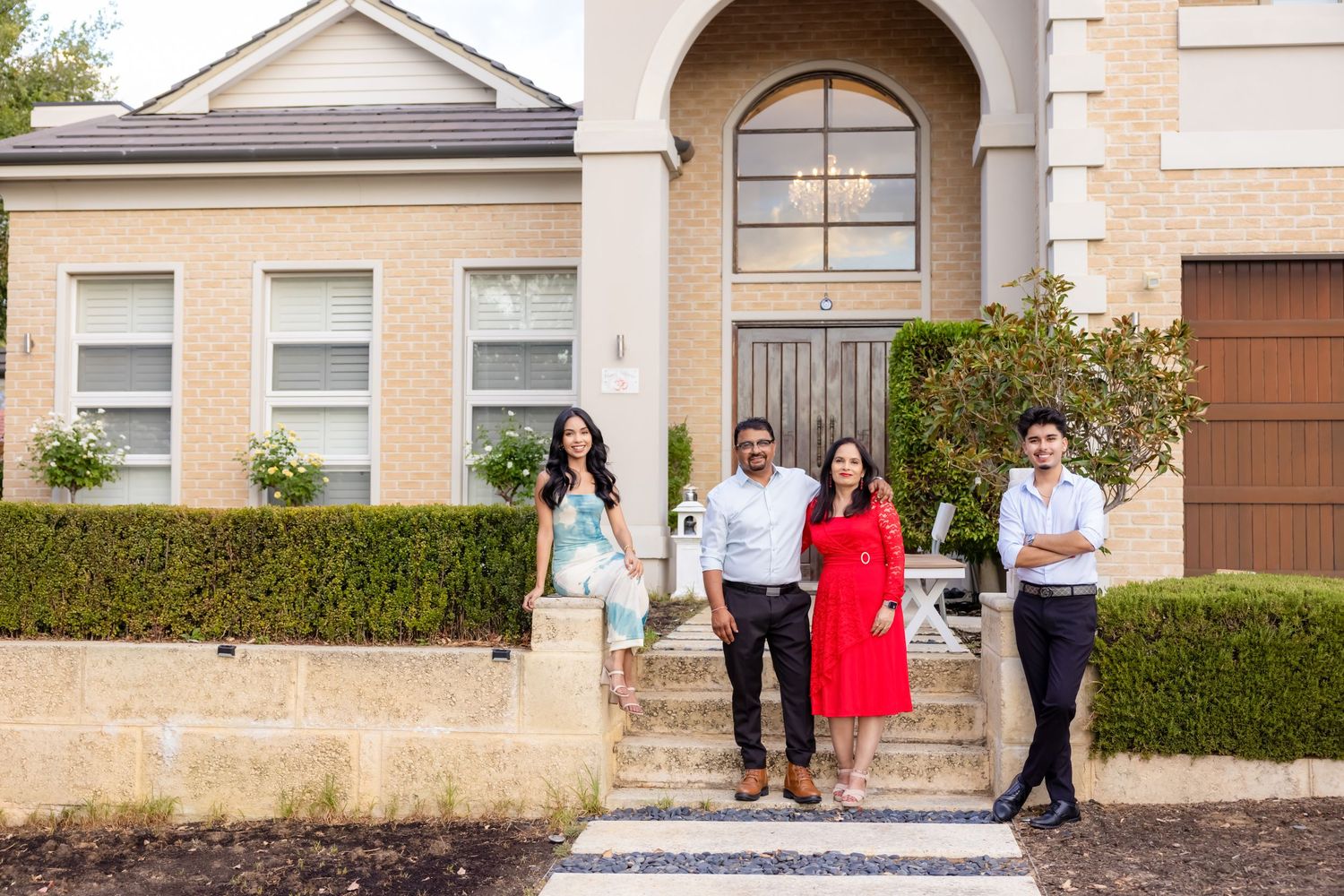 Family of four posing proudly in front of their elegant two-story brick home with grand entrance.