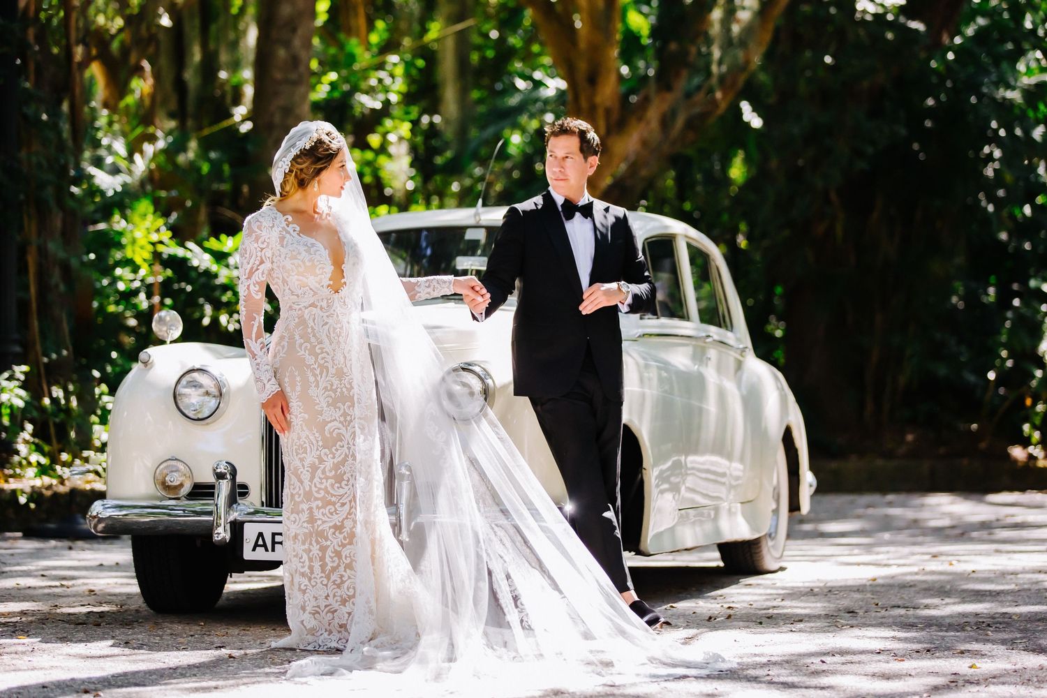 Elegant wedding photo shoot with vintage white car and garden scenery.