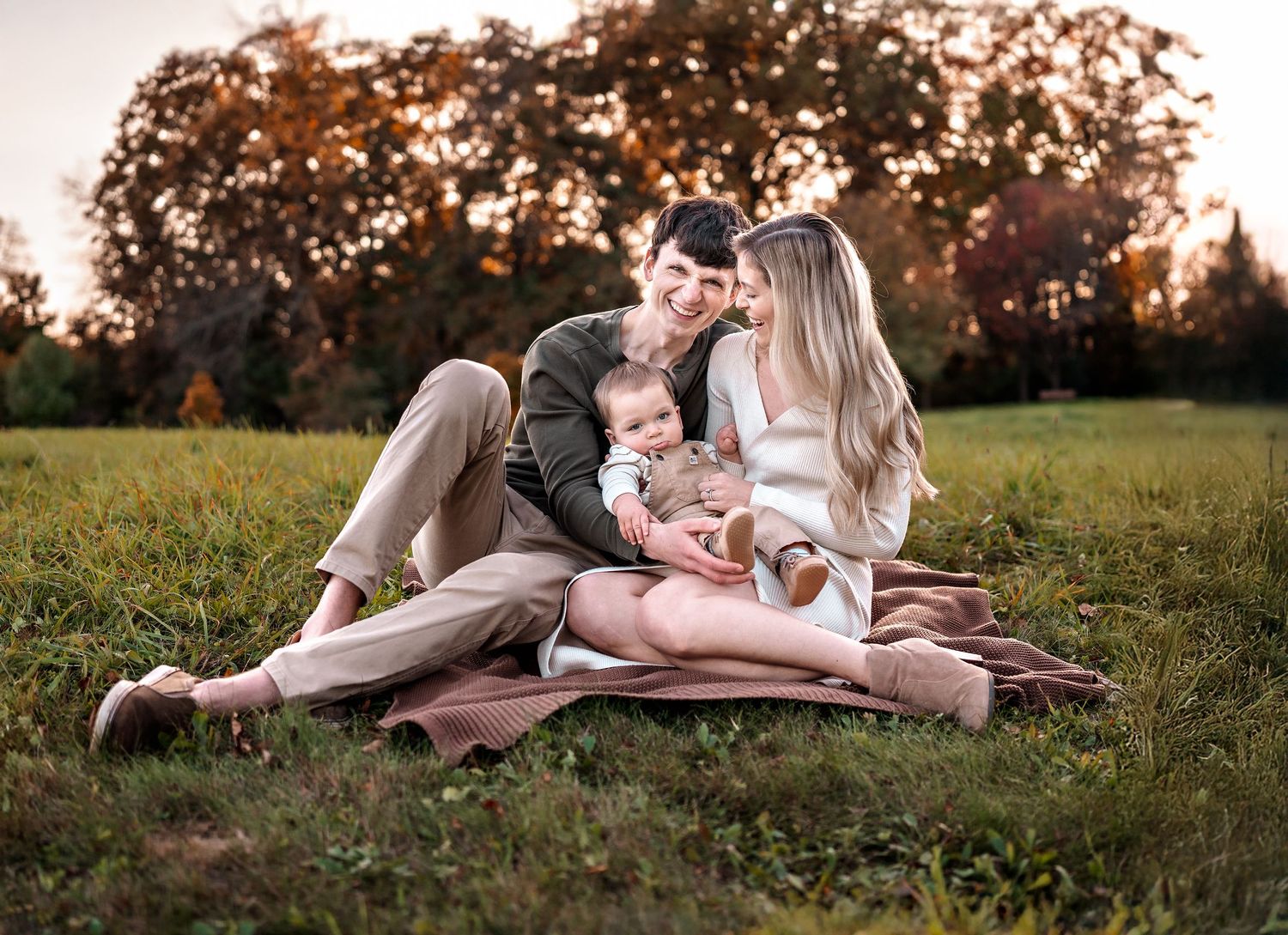 Family sitting together on a picnic blanket in a grassy field at sunset during a golden autumn evening.