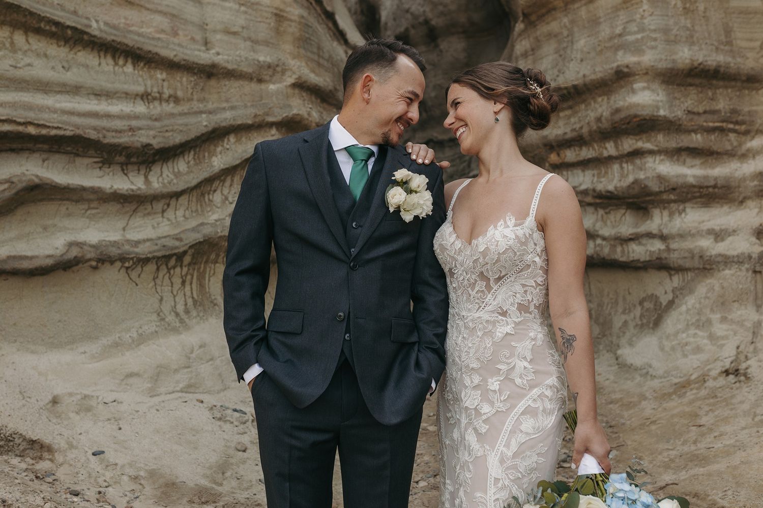 Elegant wedding couple posing against dramatic rocky cliff backdrop at Calafia Beach Park in San Clemente.