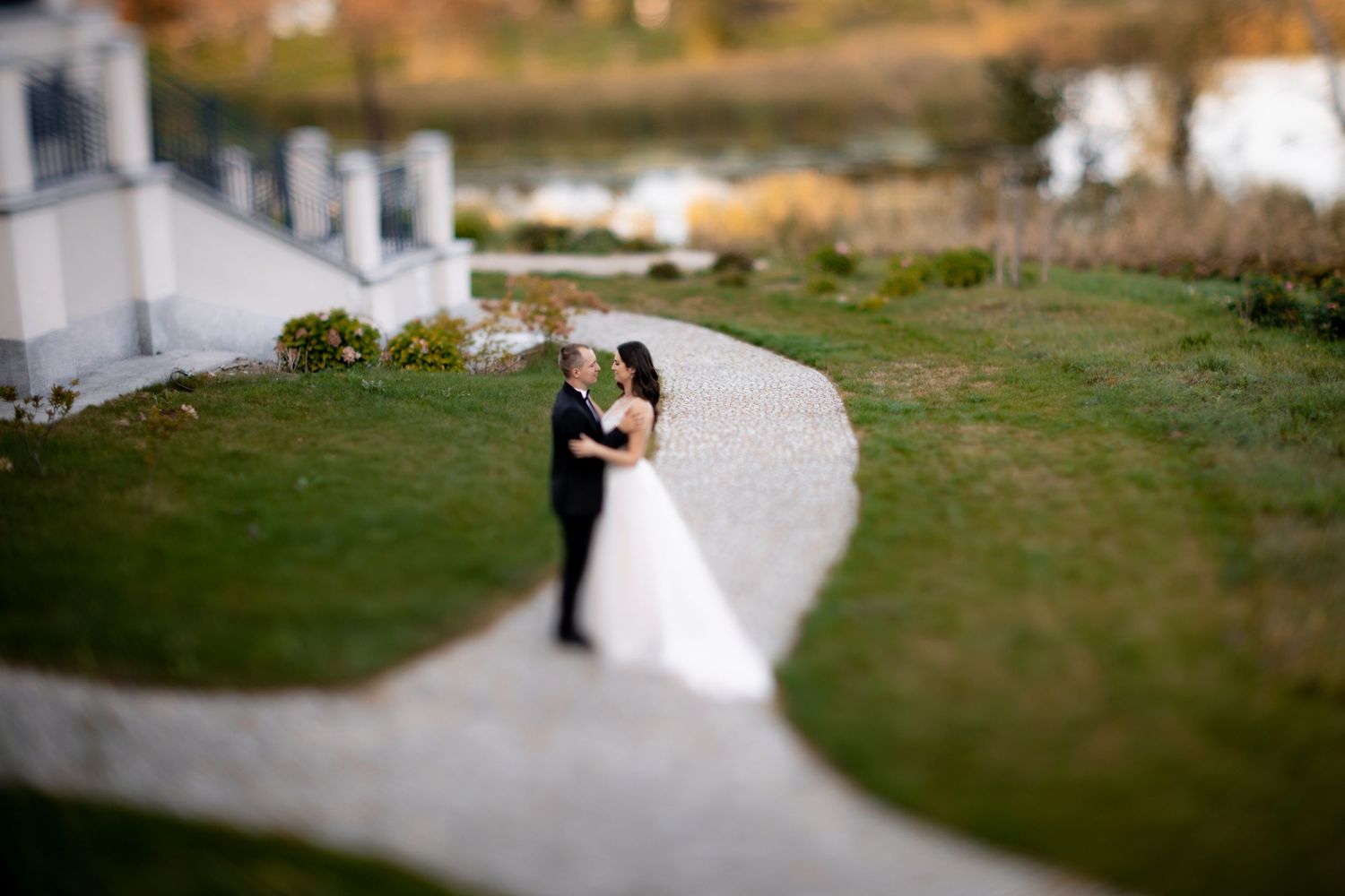 Aerial tilt-shift photo of newlyweds on a winding path surrounded by manicured lawns.