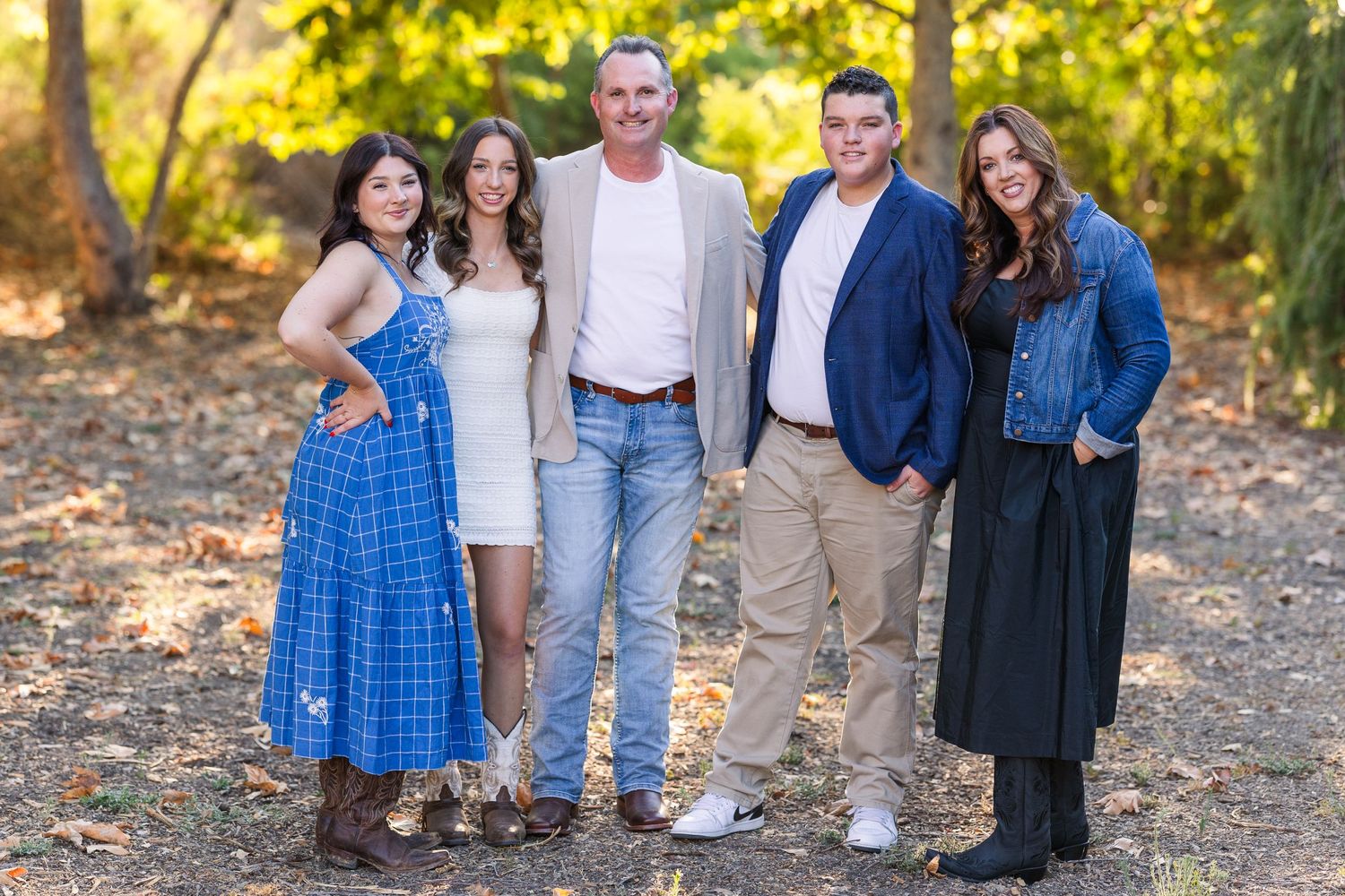 Family group poses together on an autumn path surrounded by golden leaves.