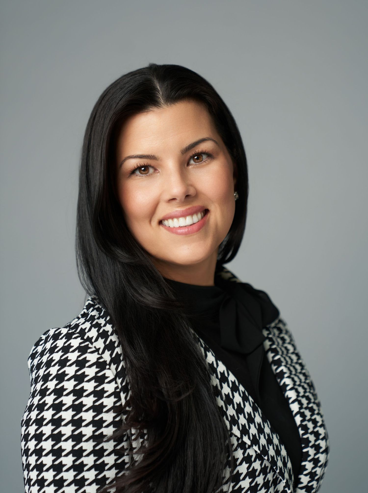 Professional headshots in houndstooth jacket with black turtleneck against gray backdrop.