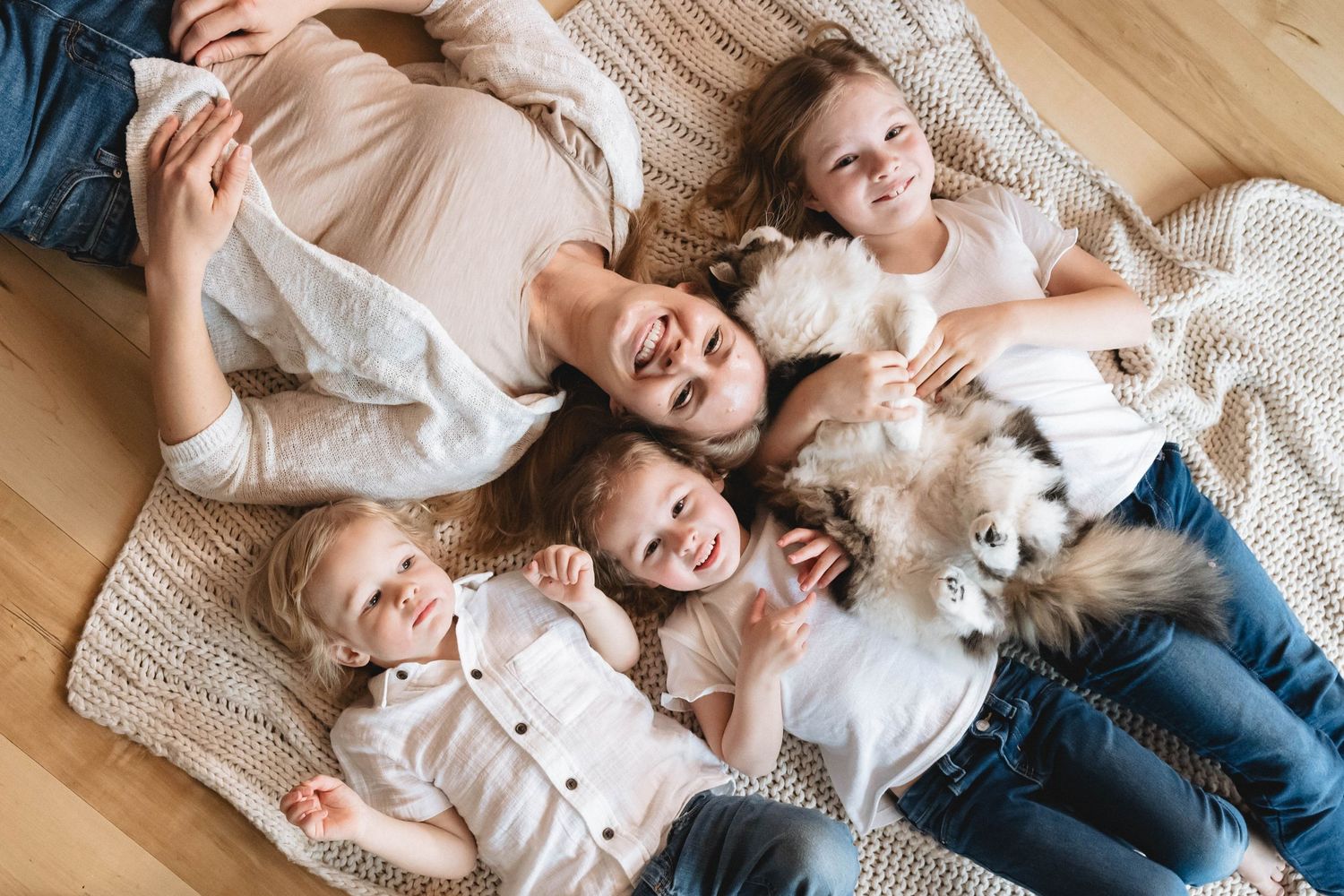 Happy family with four children and fluffy cat lying together on cozy blanket on floor.