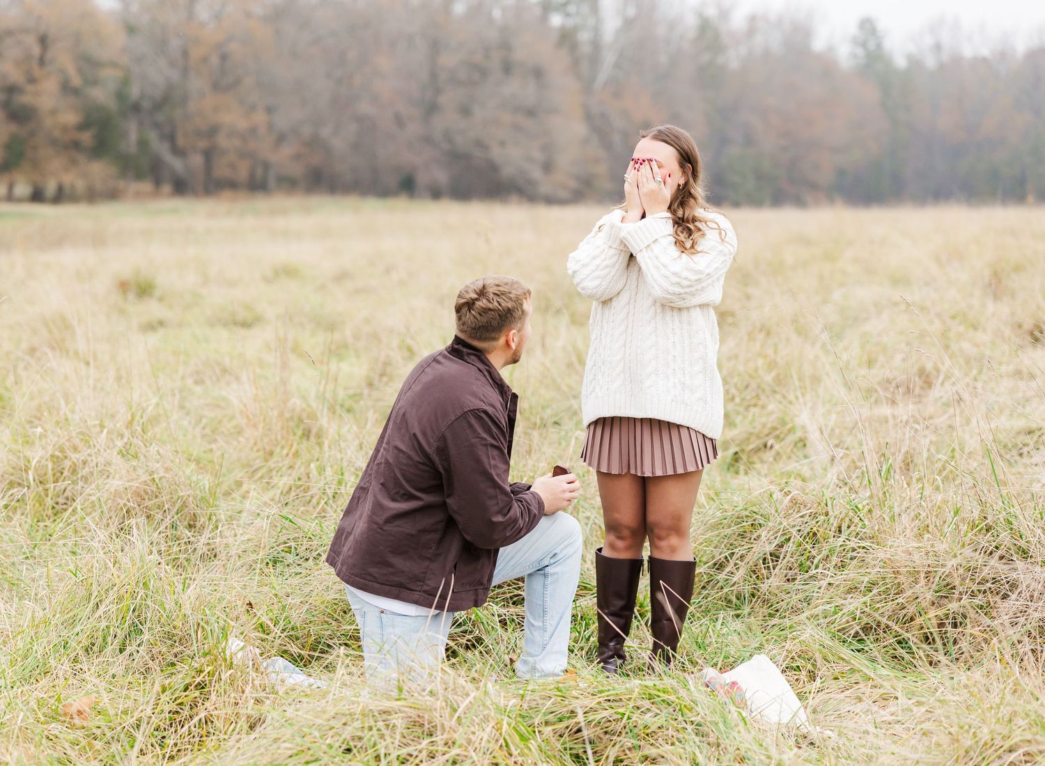 Two people share a special moment during a proposal in a misty autumn field with tall grass.