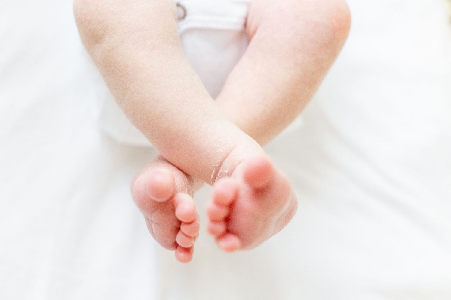 Close up view of tiny baby feet on white blanket showing soft pink soles. Augusta baby photographer.