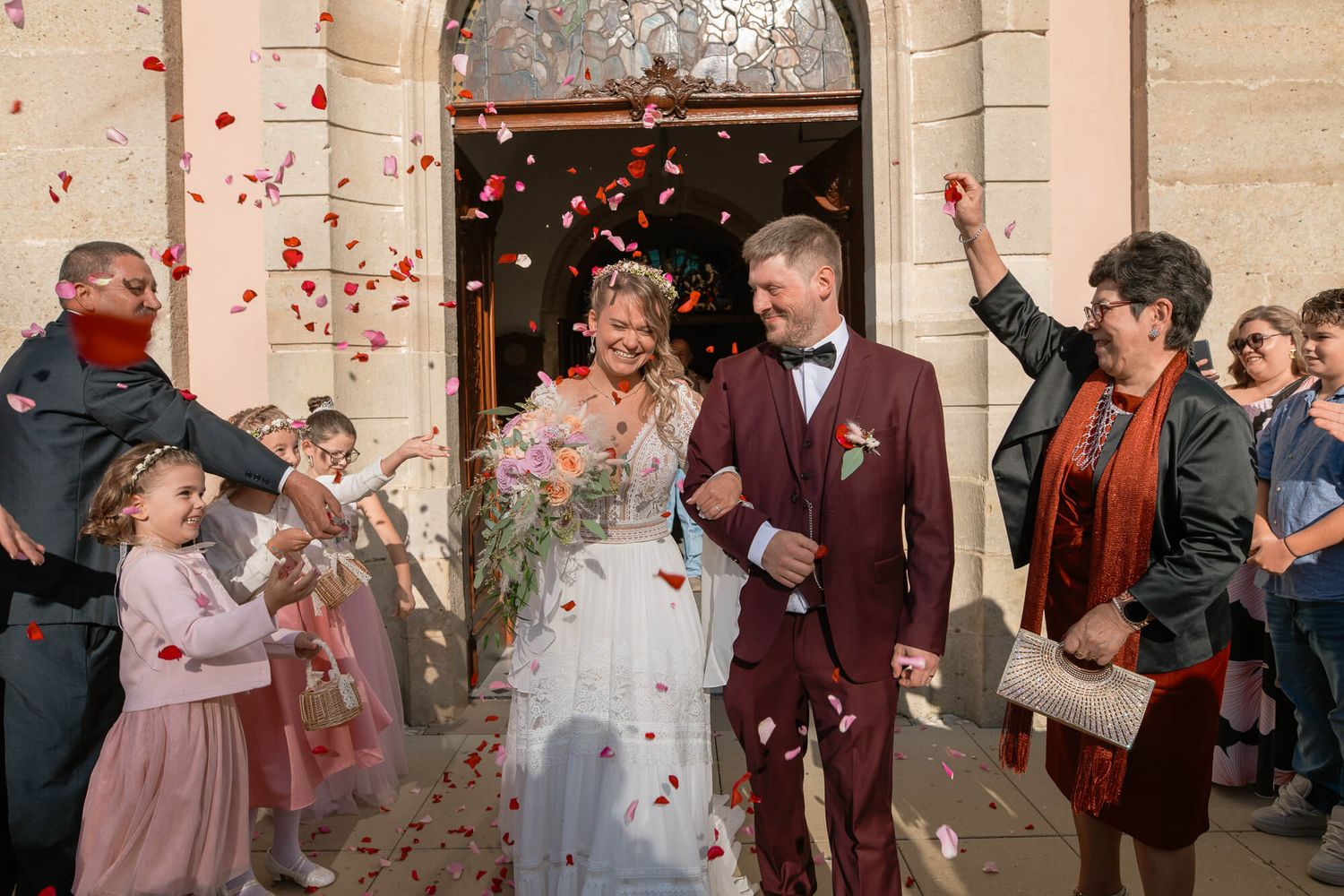 A wedding couple exits a church doorway while guests shower them with pink rose petals in celebration.
