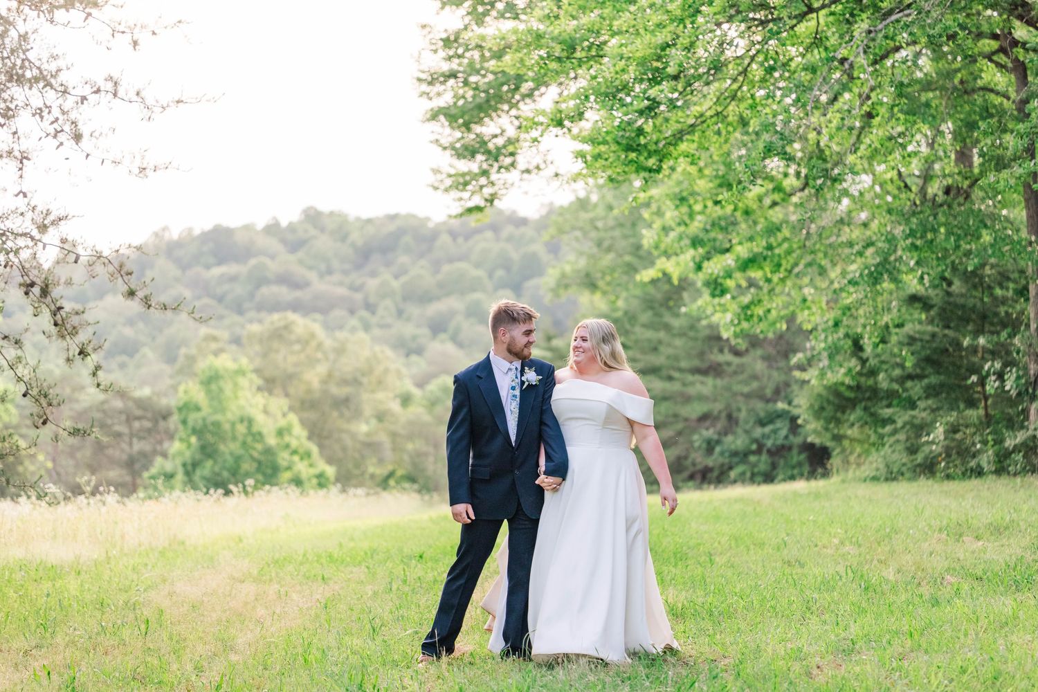 A couple poses together on a grassy hillside in wedding attire on their special day.