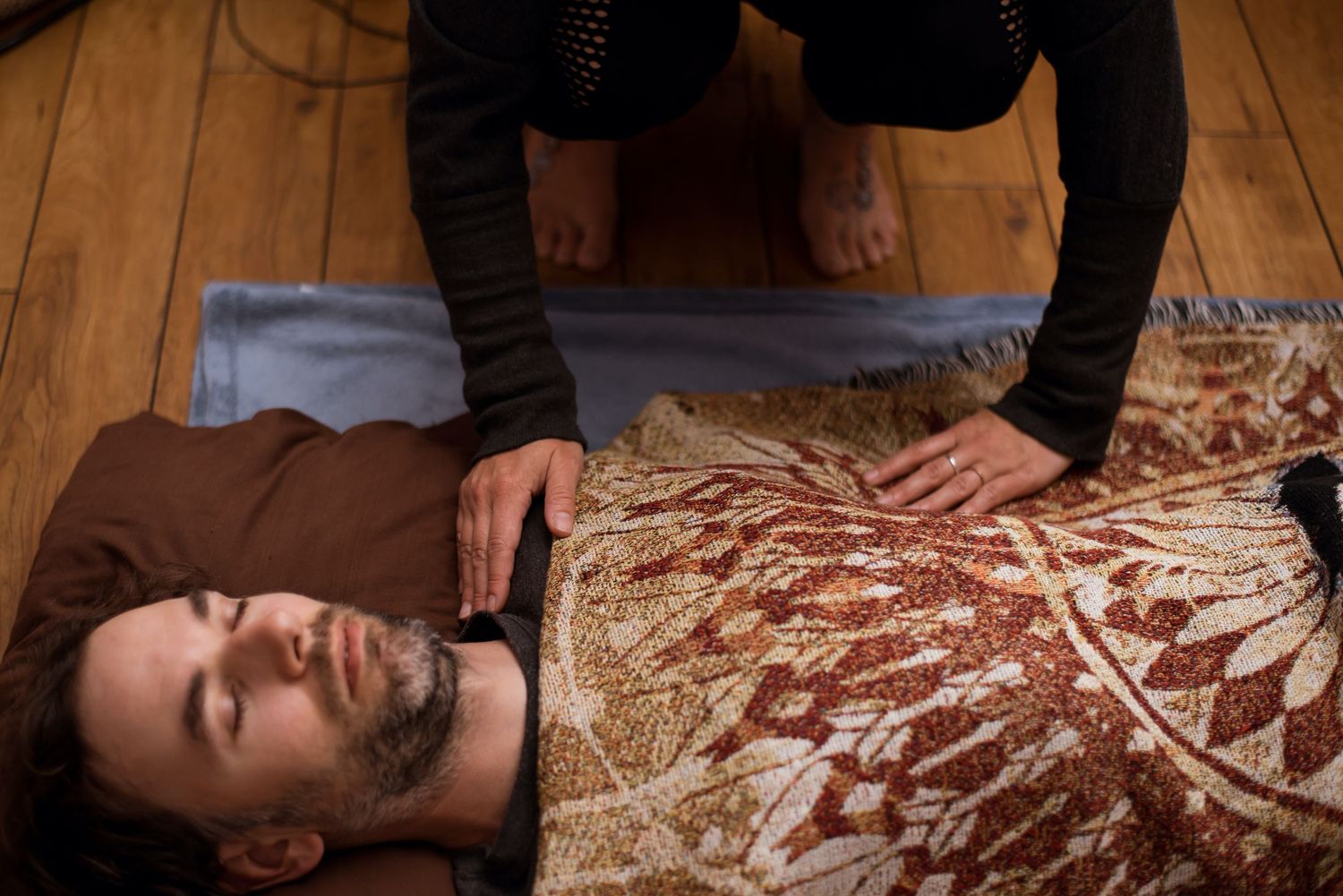 Person receiving a relaxing therapeutic treatment on hardwood floor with patterned blanket.