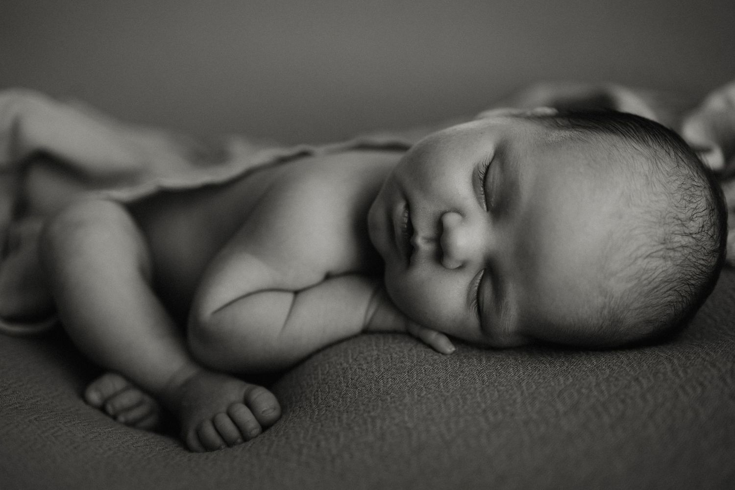 Sleeping newborn curled up on brown fabric in artistic pose.