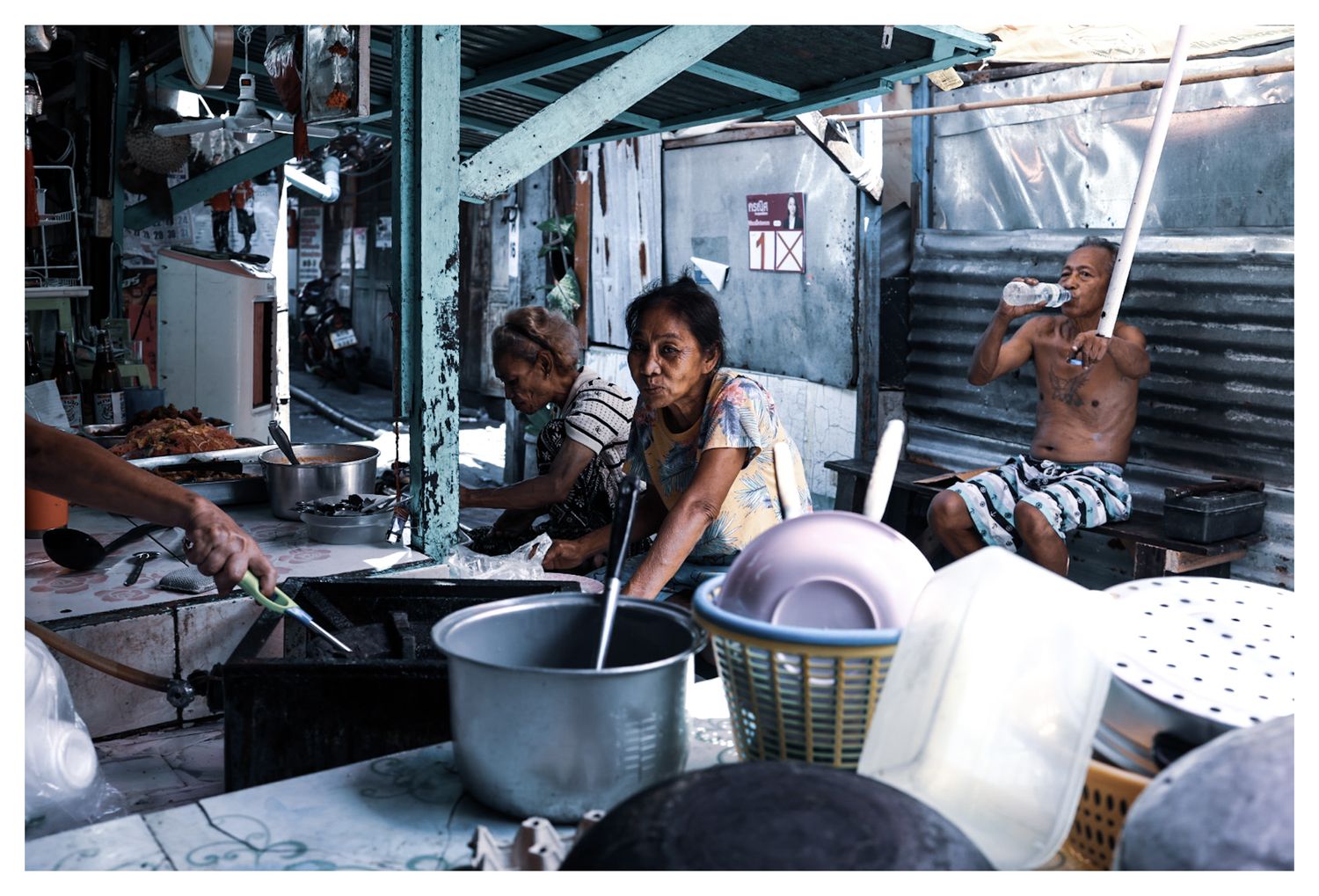 Street food vendors cooking in an outdoor market stall with large pots and baskets in Asia.
