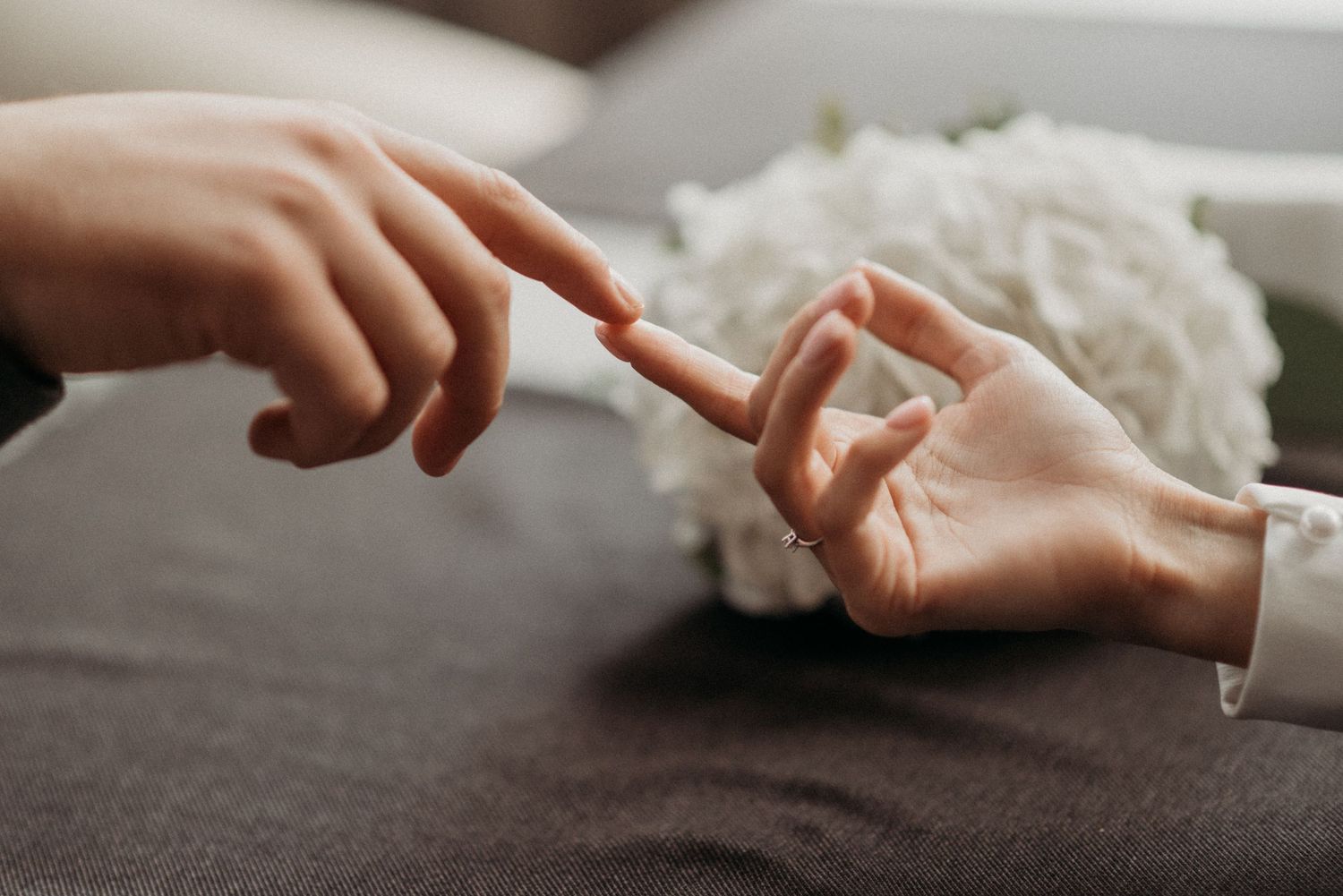 Two hands reaching towards each other in an intimate gesture against a soft background.