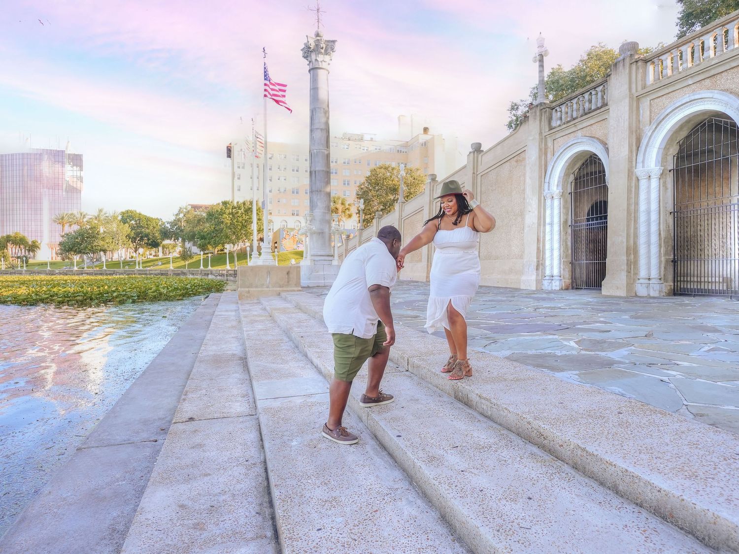Couple in white outfits dancing together on waterfront promenade during sunset.