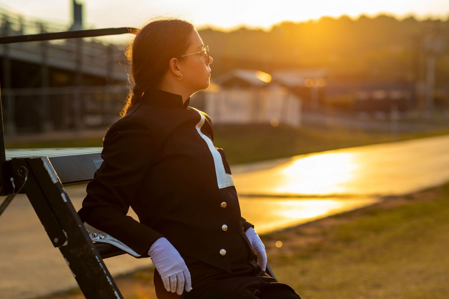 Silhouetted figure in black coat sits on bench during golden sunset.