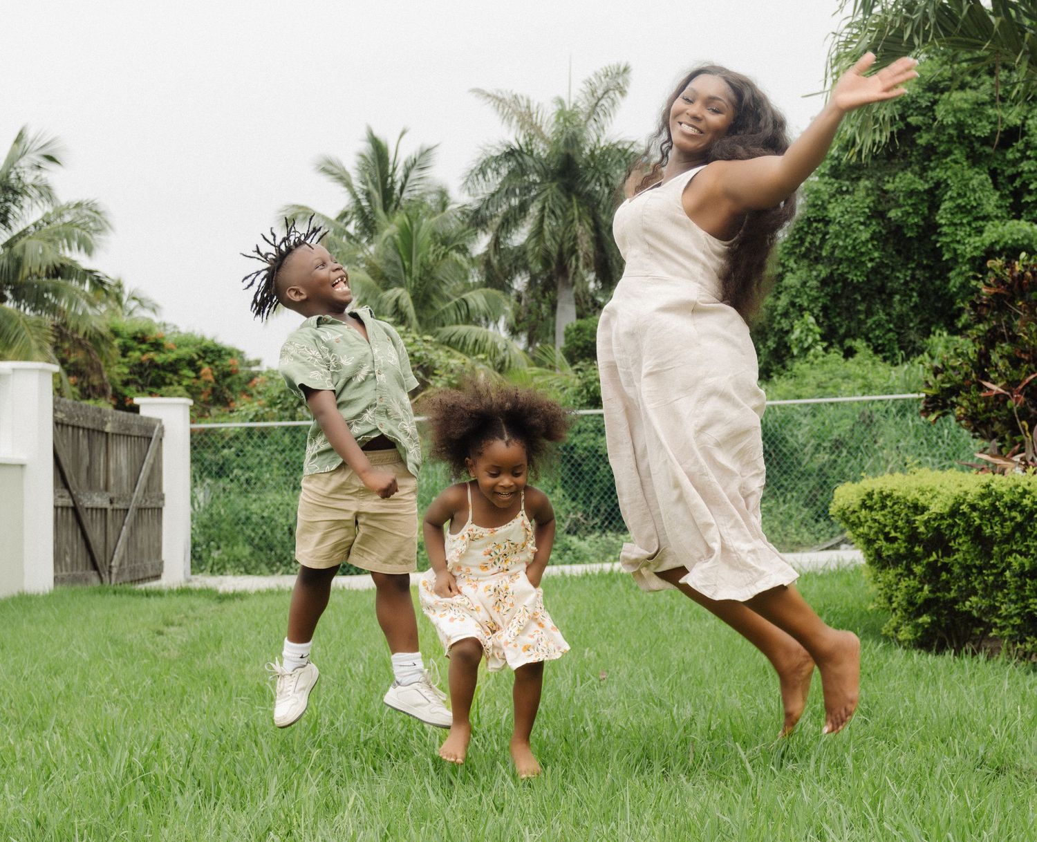 Family jumps with joy together on a lush green lawn with palm trees in the background.