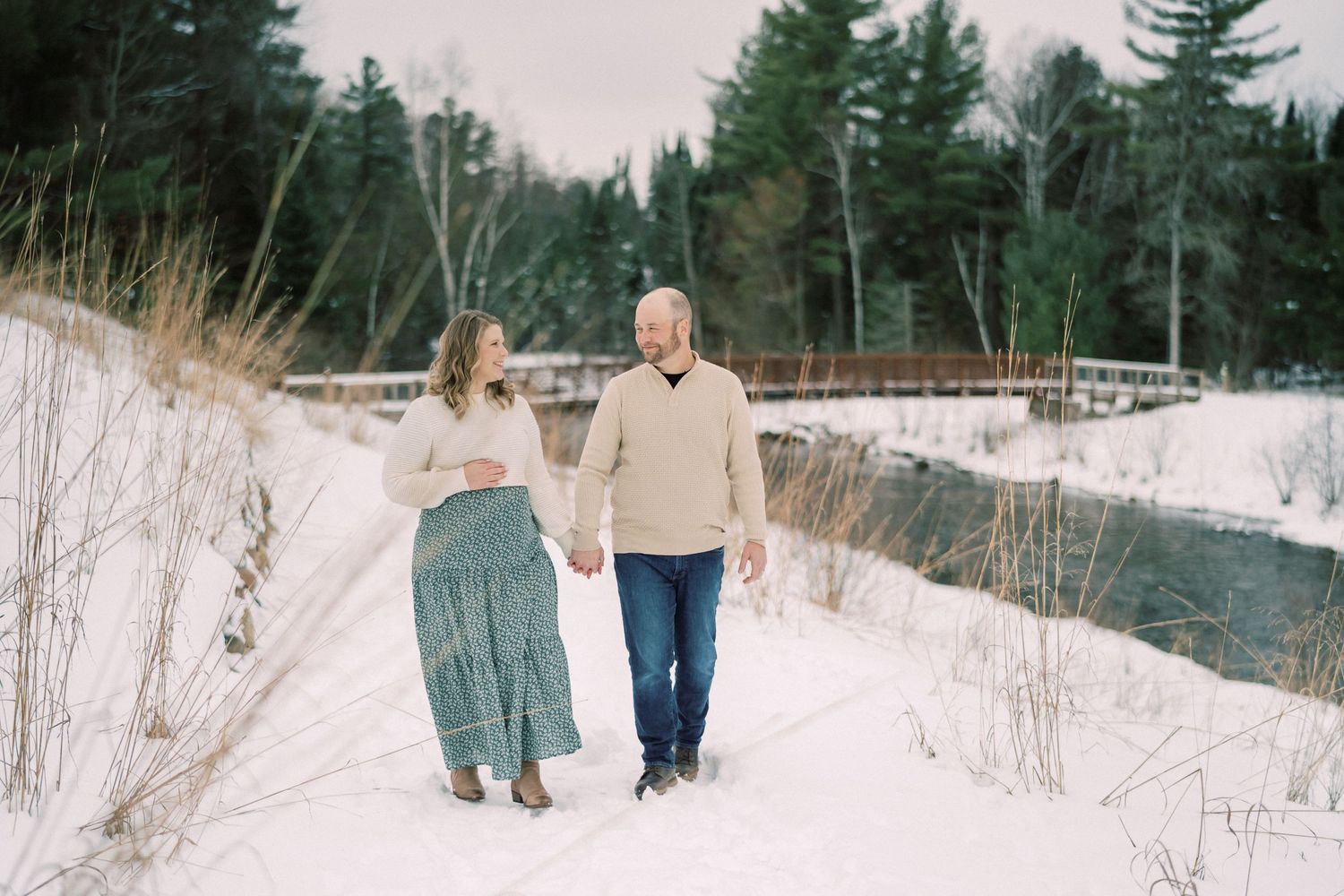 Couple walking together on a snowy path with evergreen trees in the background.