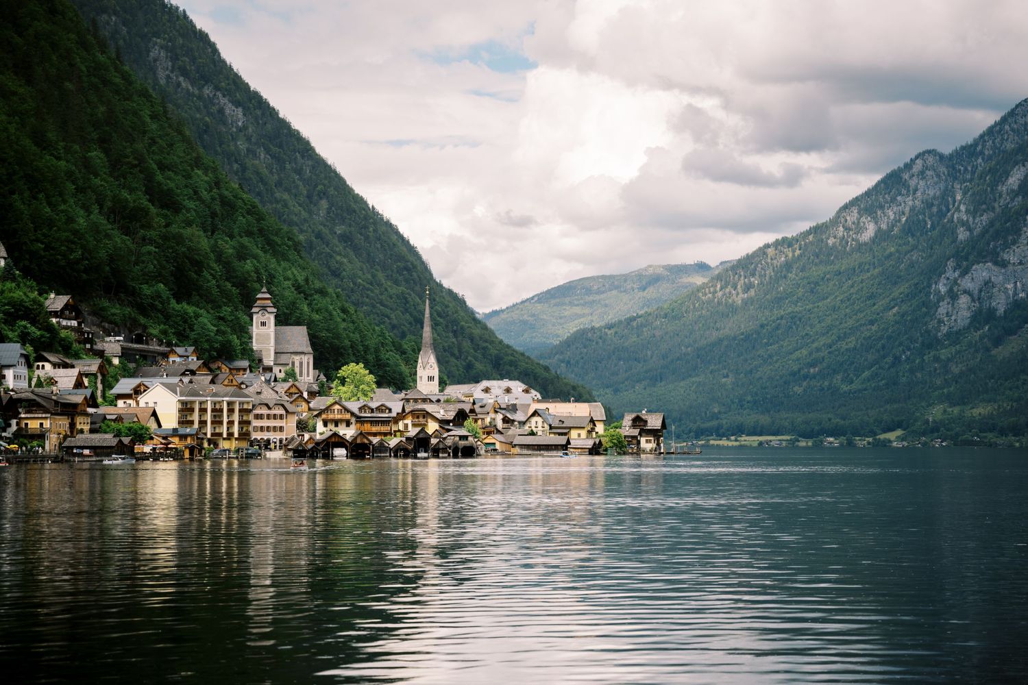 Scenic view of Hallstatt village nestled between mountains along Lake Hallstatt in Austria with church spires and reflective waters.