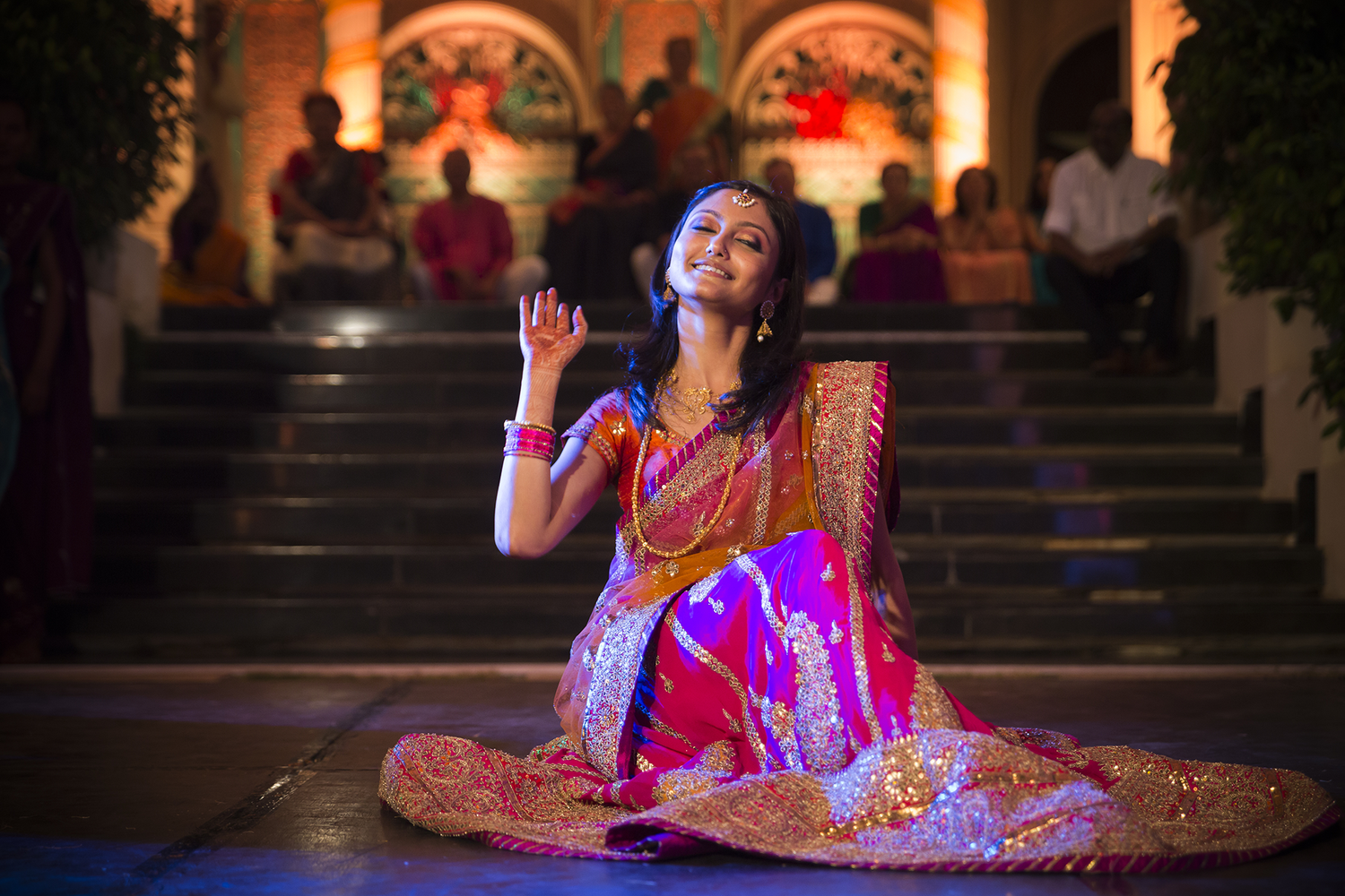 A dancer in traditional Indian attire performs under colorful lights on stone steps.