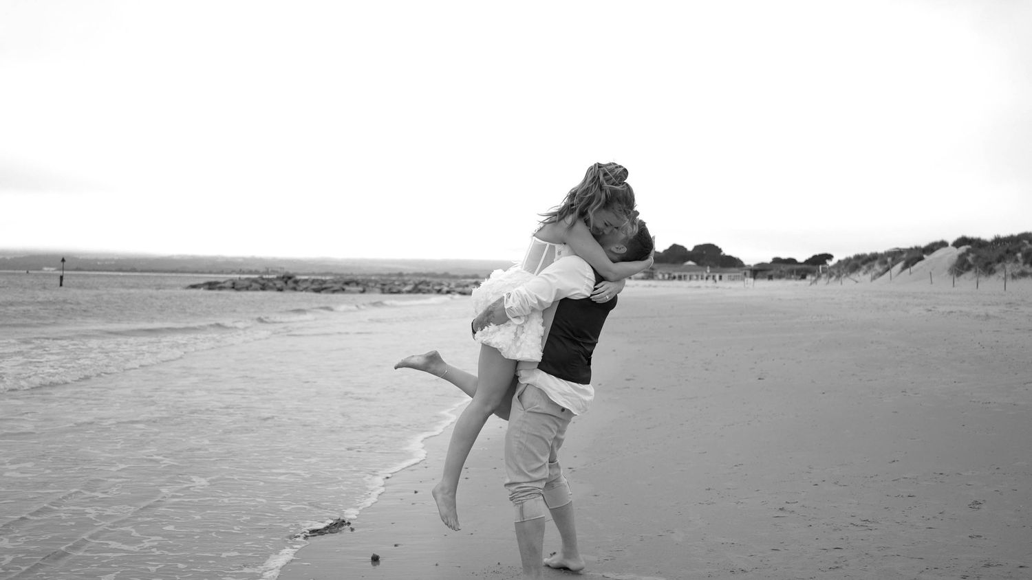 A couple embraces romantically on an empty beach with the waves and horizon in the background.
