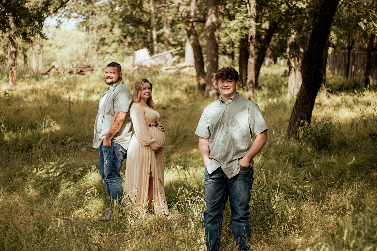 Group of people pose together in a sunlit wooded area with tall trees and natural lighting.